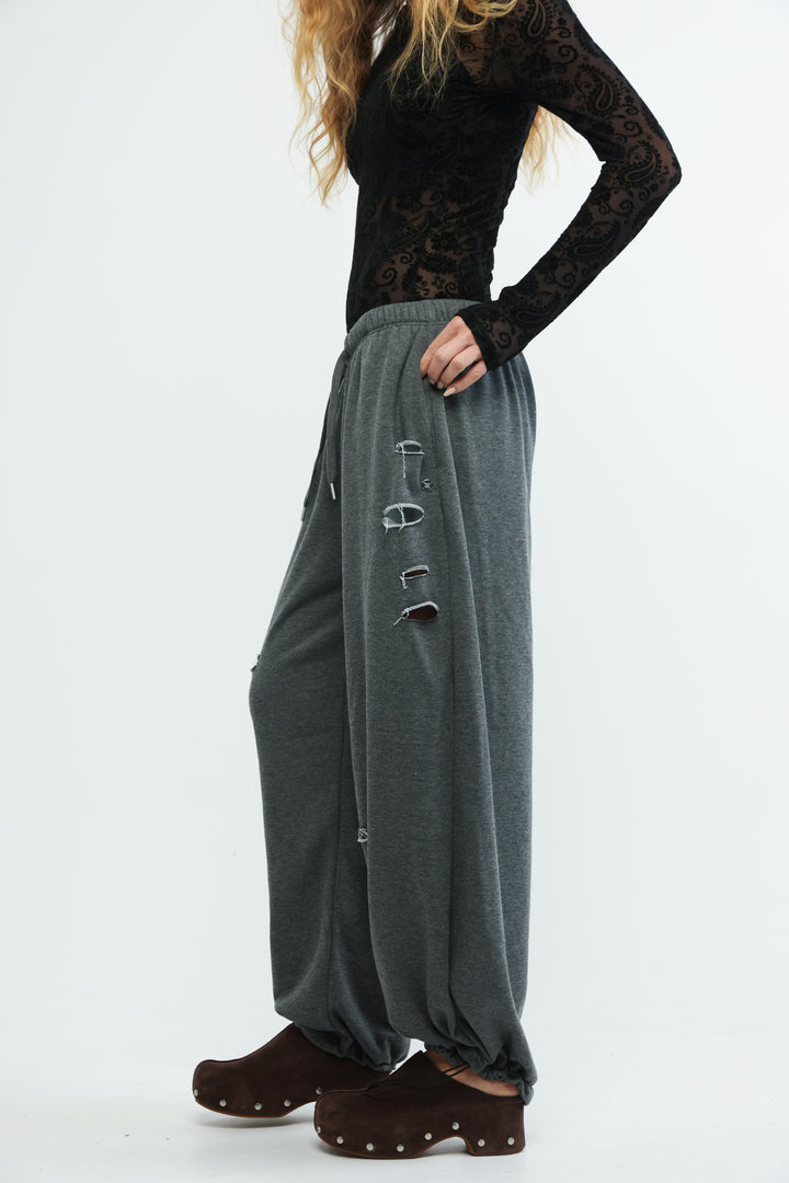 Dark gray loose-fitting harem pants with distressed holes along the side seam shown from the front angle