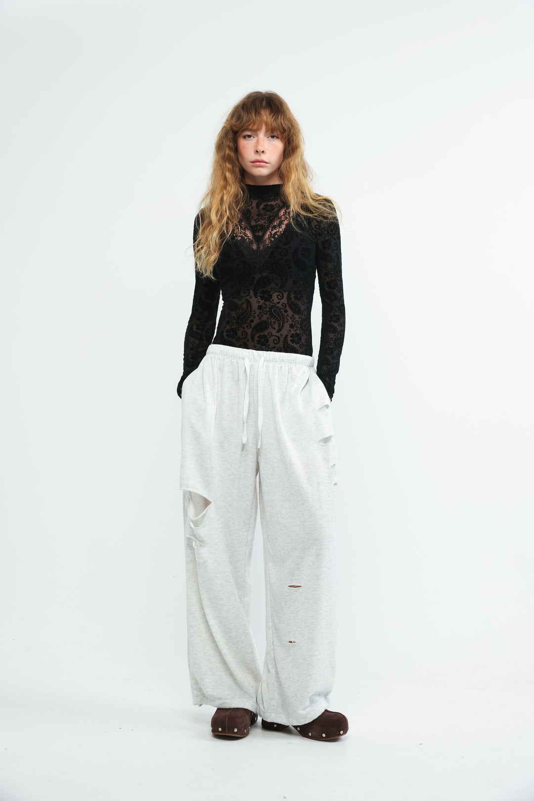 Front view of scissors grey joggers paired with a black lace long-sleeve top with high neckline and patterned details