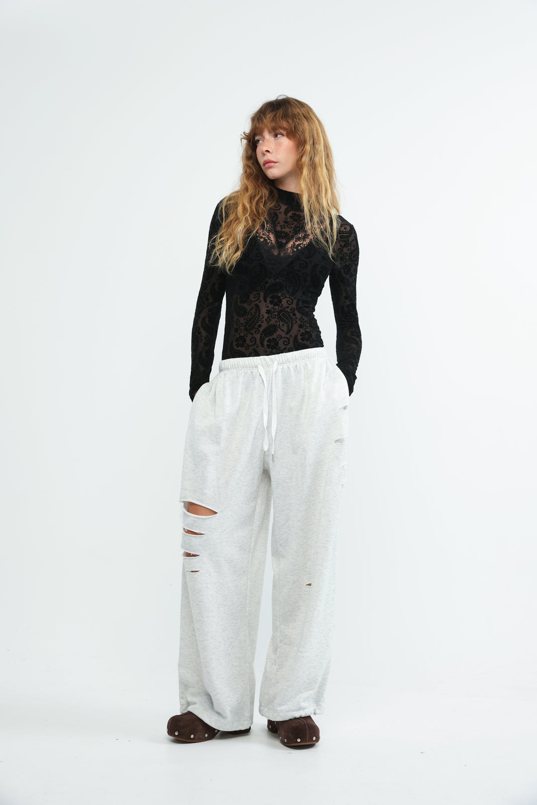 A front view of scissors grey joggers paired with a black lace long-sleeved top featuring a high neckline and floral patterns