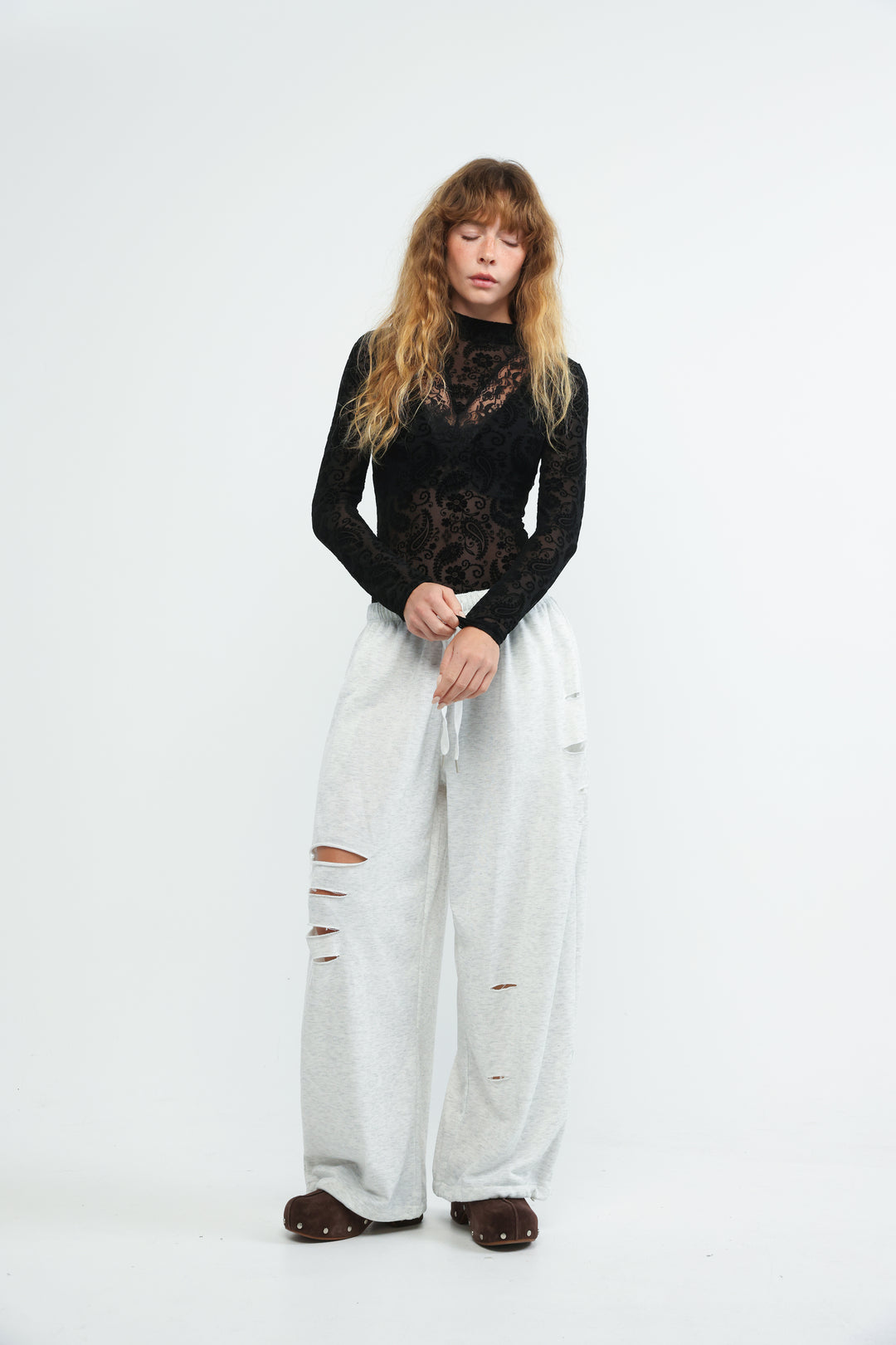 A woman wearing a black lace long-sleeve claim black bodysuit with wide-leg ripped jeans and brown studded shoes