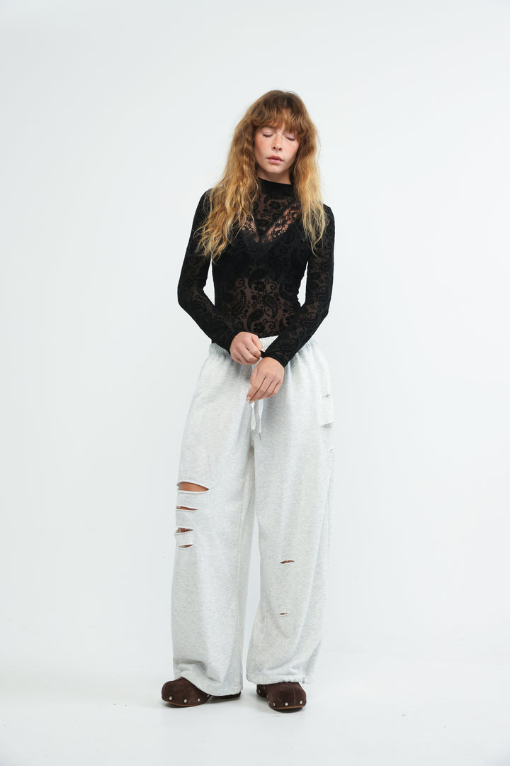 A woman wearing a black lace long-sleeve claim black bodysuit with wide-leg ripped jeans and brown studded shoes