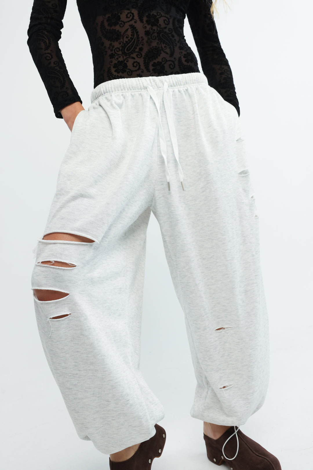 Light gray scissors grey joggers with loose fit and distressed ripped details on thighs and knees front view