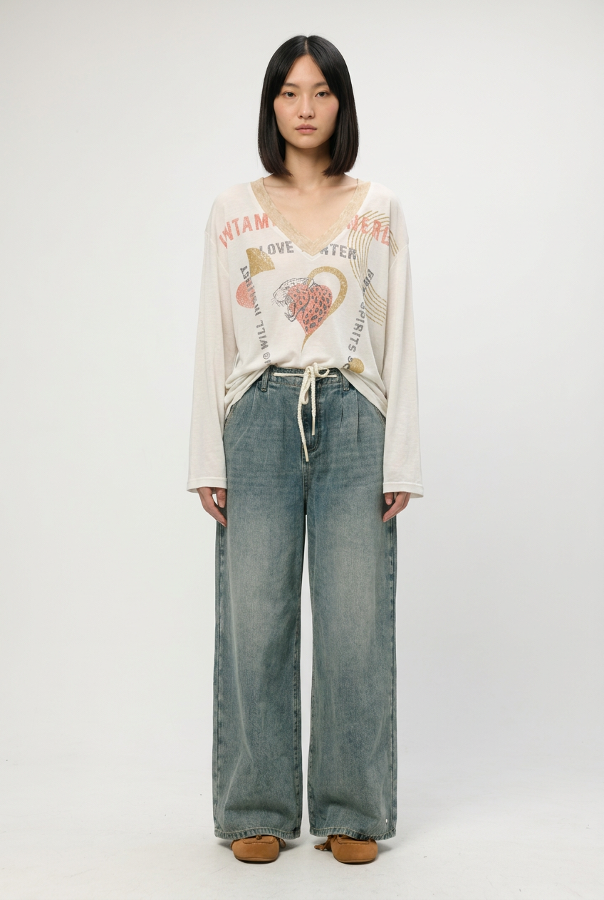 White long-sleeved v-neck graphic tee with colorful text and heart design paired with blue denim shown from front