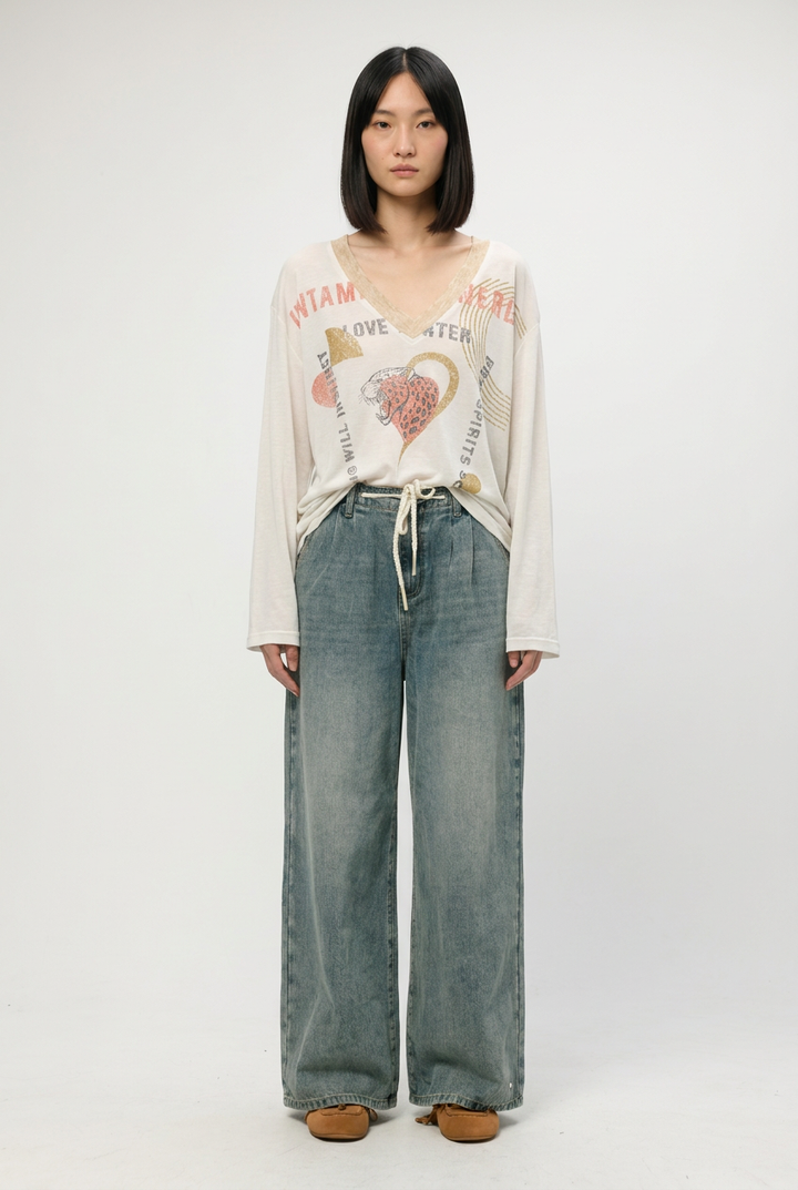 White long-sleeved v-neck graphic tee with colorful text and heart design paired with blue denim shown from front