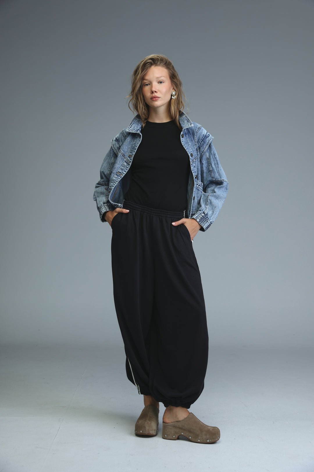 Woman wearing ballooning black striped joggers with side stripes paired with brown clog-style shoes and denim jacket