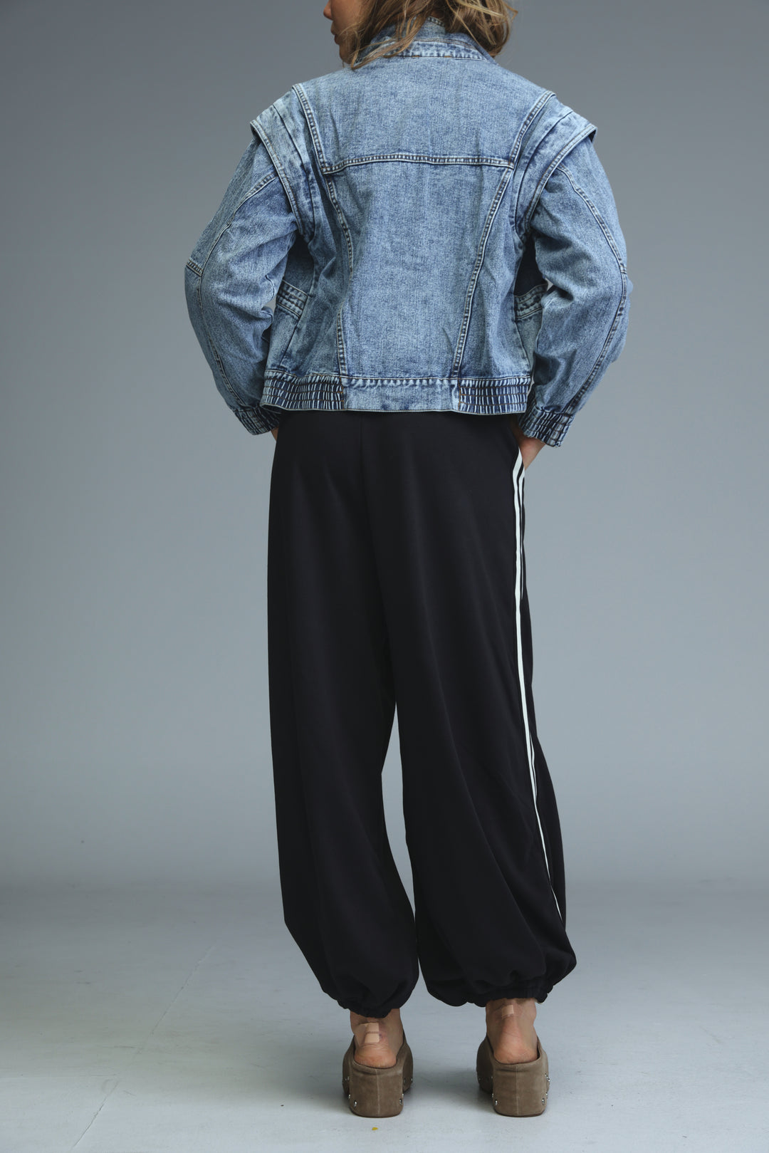 Light-wash denim jacket with relaxed fit and rolled-up sleeves paired with ballooning black striped joggers front view