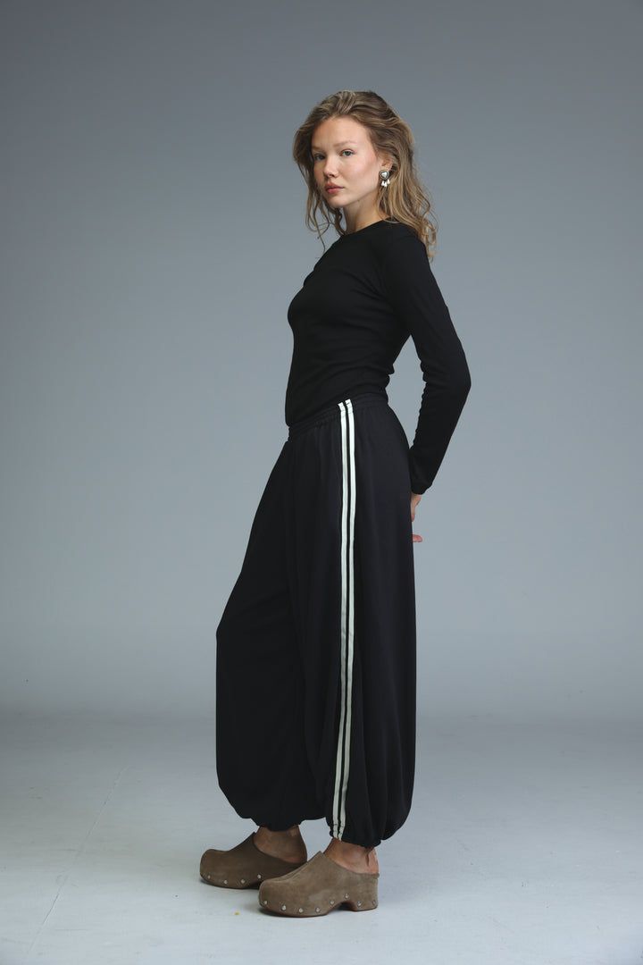 Ballooning black striped joggers with wide legs and two vertical white stripes down the sides shown from the front