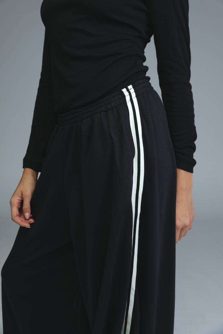 Black ballooning joggers with wide legs and two vertical white stripes down the sides front view