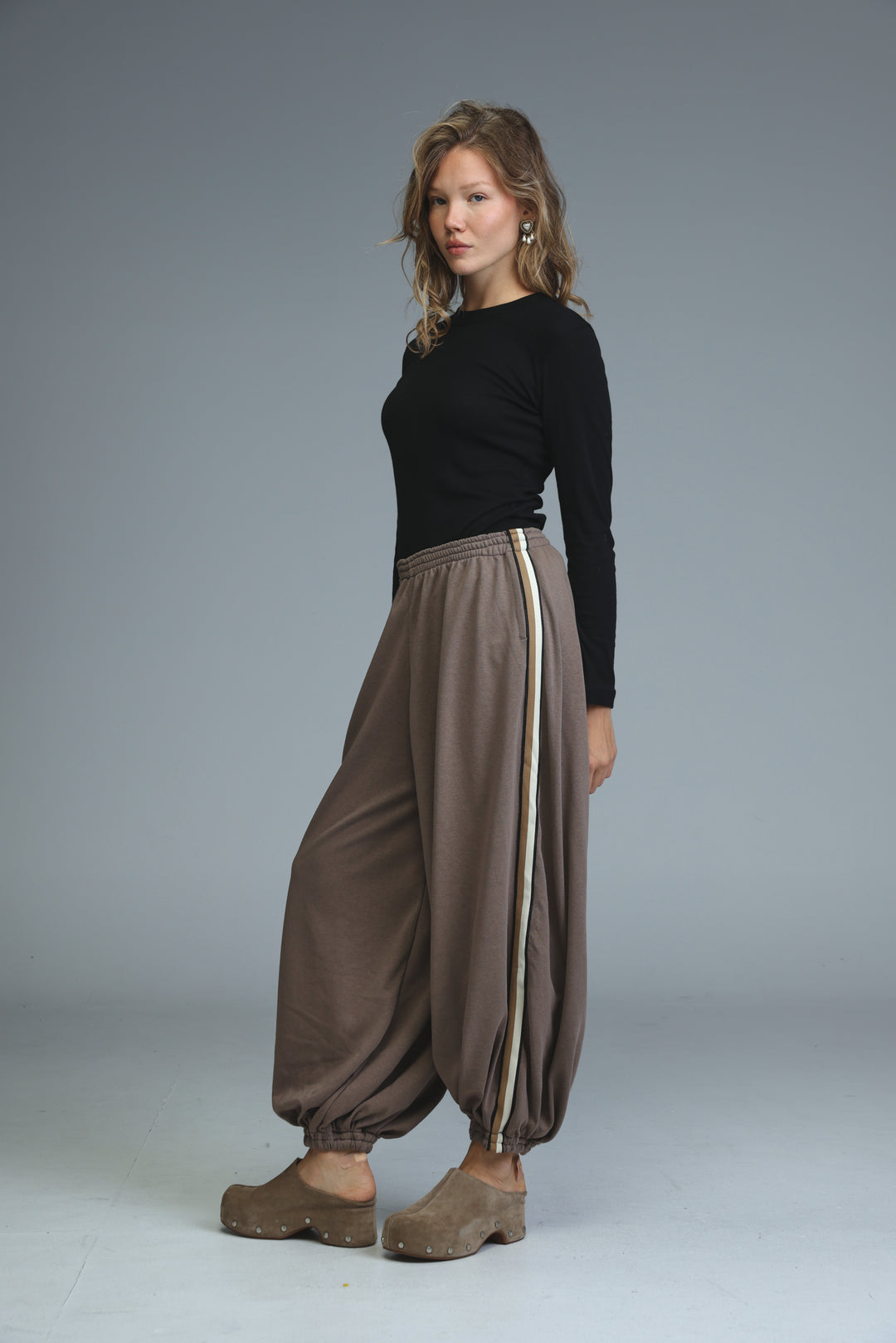Brown loose-fitting harem pants with a vertical beige stripe down the side shown from the front