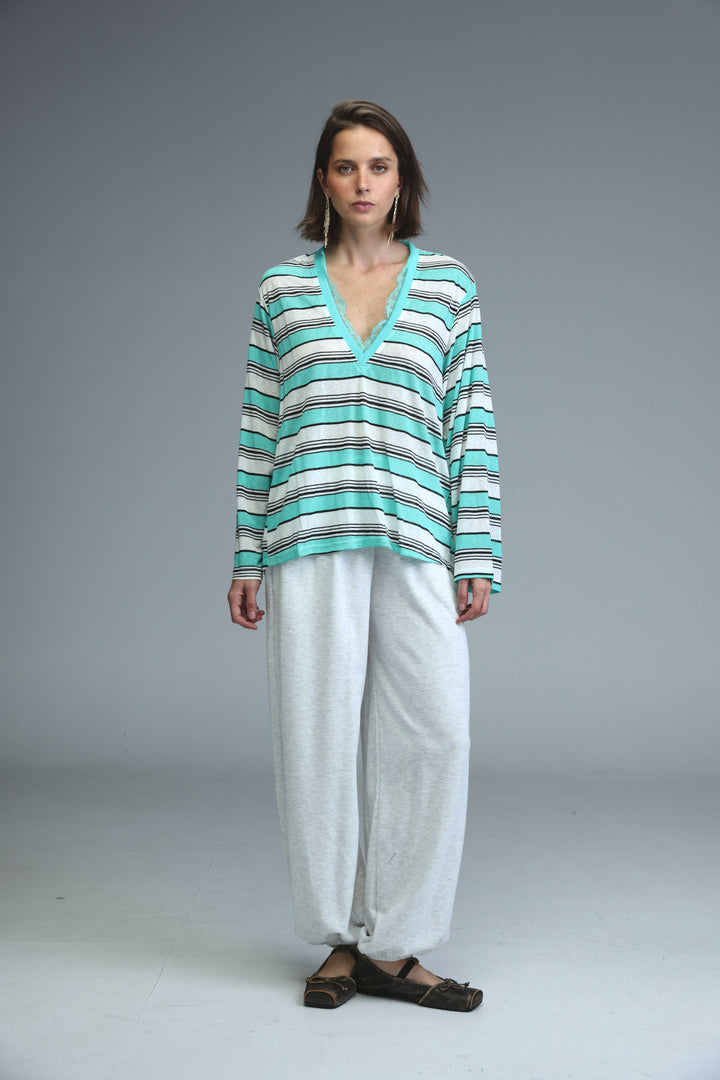 A woman wearing a glow mint long-sleeved v-neck striped shirt with teal, white, and black horizontal stripes