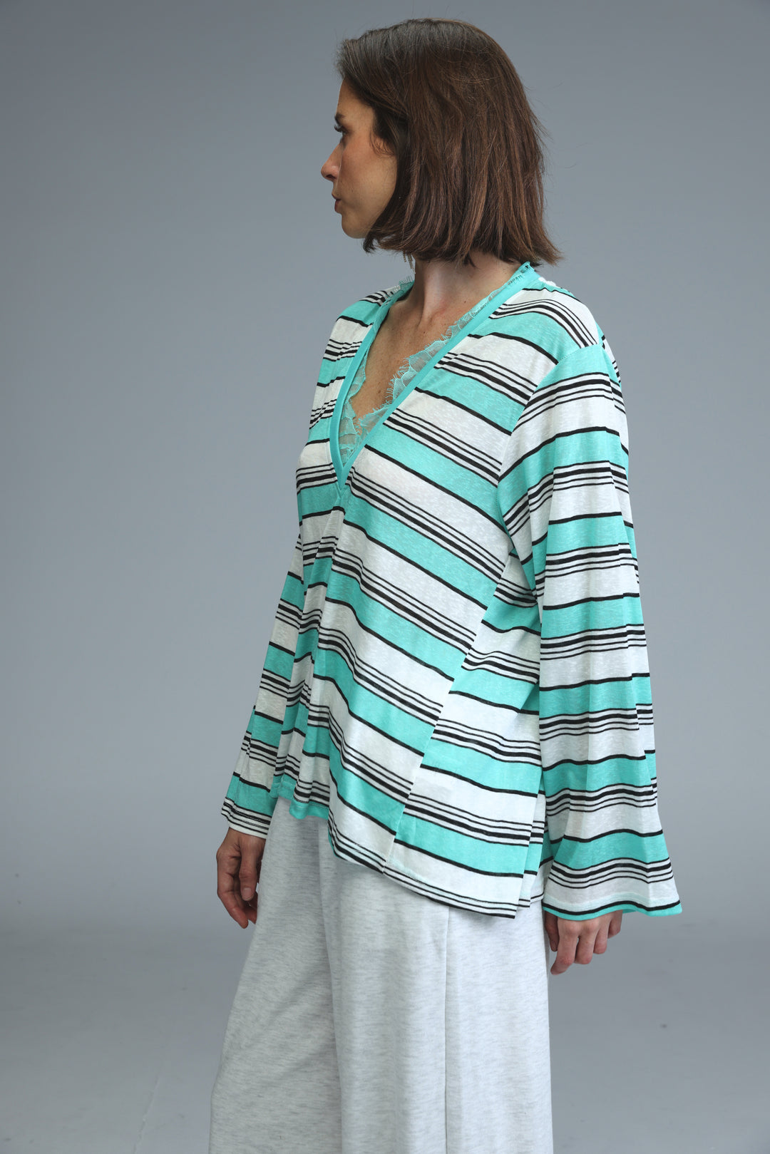 A woman wearing a front view of a glow mint striped shirt with teal, white, and black horizontal stripes and v-neckline