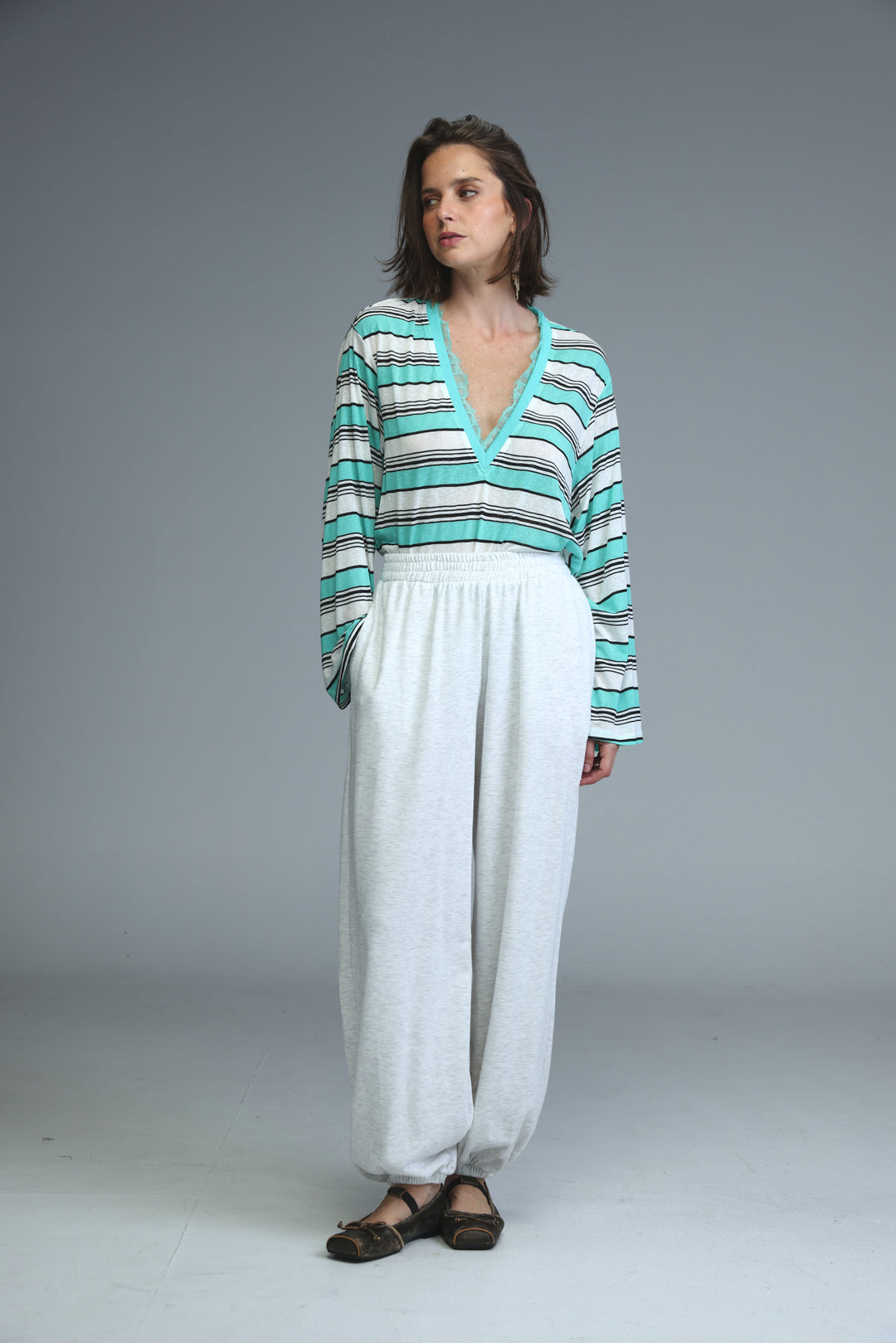 A woman wearing teal and white striped long-sleeved v-neck top paired with light grey joggers shown from the front