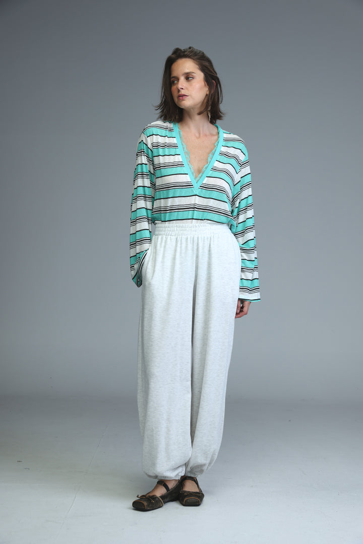 A woman wearing teal and white striped long-sleeved v-neck top paired with light grey joggers shown from the front