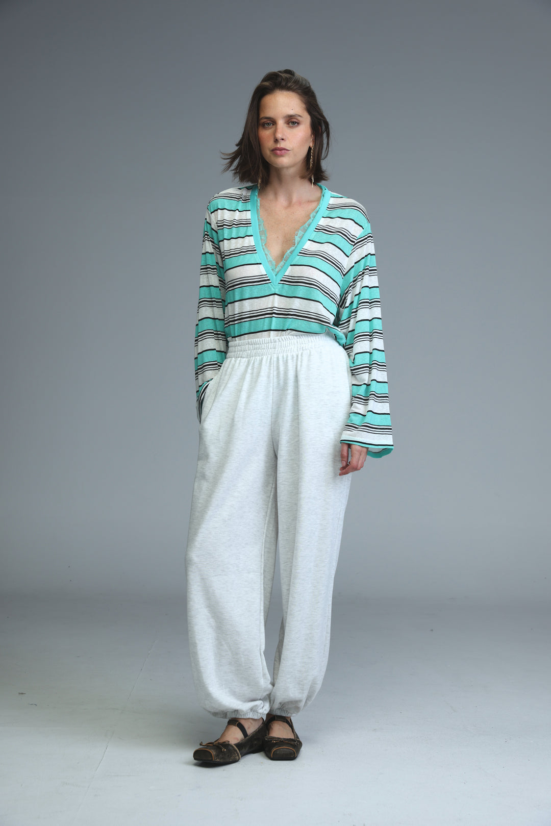 Woman wearing long-sleeved v-neck top with teal white and black stripes paired with light grey joggers front view