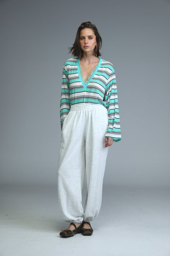 Woman wearing long-sleeved v-neck top with teal white and black stripes paired with light grey joggers front view