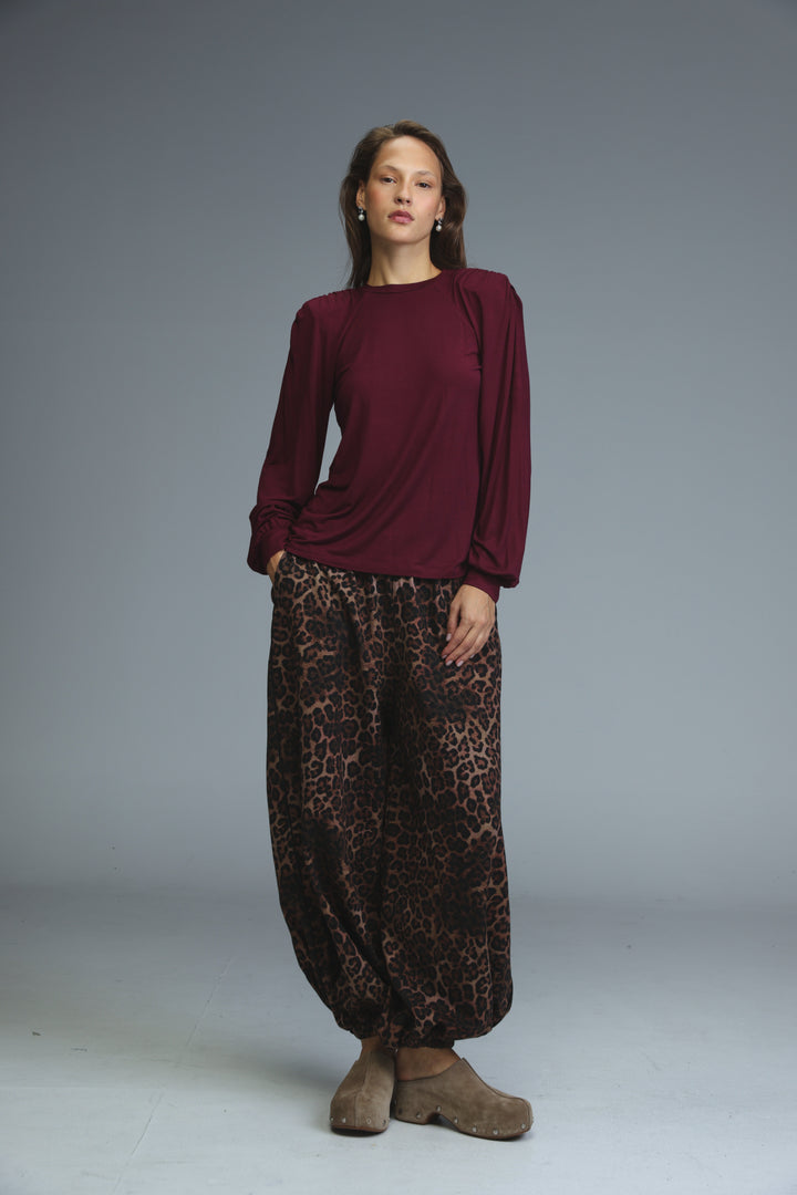 A woman wearing a front view of a maroon lg wine padded shirt with puffed shoulders paired with wide-leg pants