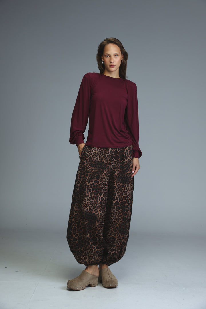 A woman wearing a maroon long-sleeved LG wine padded shirt paired with wide-leg leopard-print pants and tan shoes