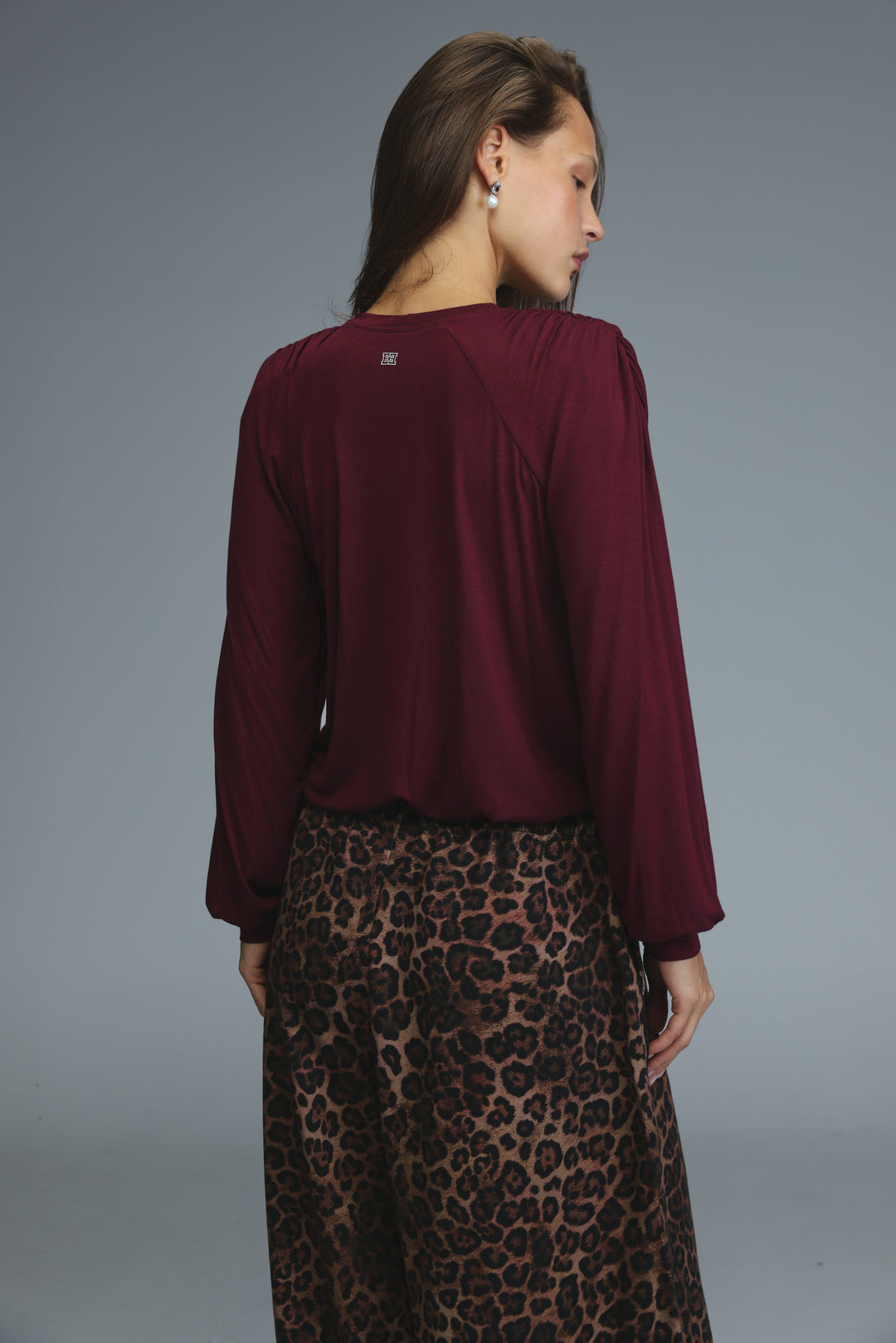 A woman wearing a maroon long-sleeved wine padded shirt with puffed sleeves and subtle back detail visible from the side