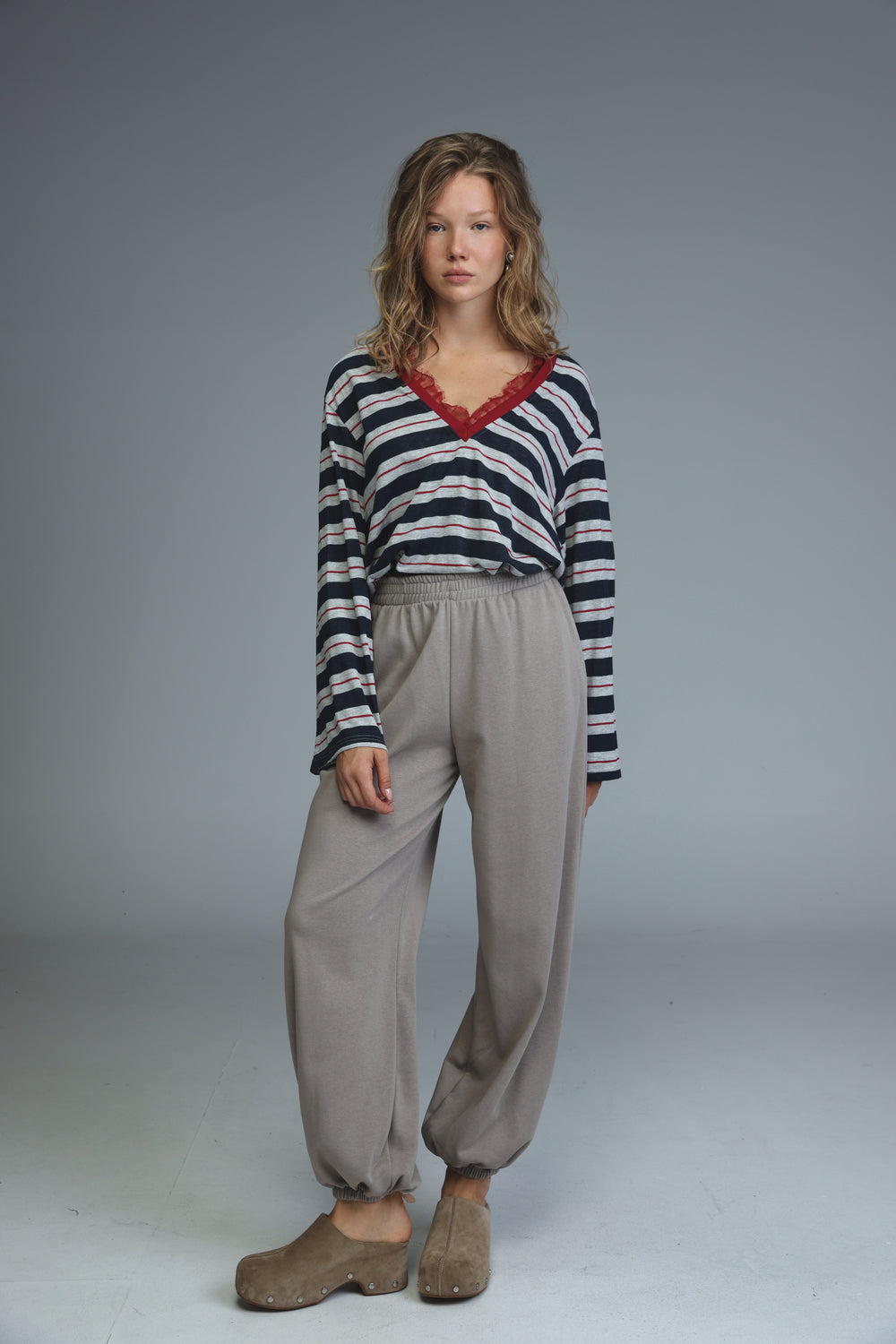 A woman wearing beige joggers with a navy and white striped long-sleeved top with red lace trim at the neckline