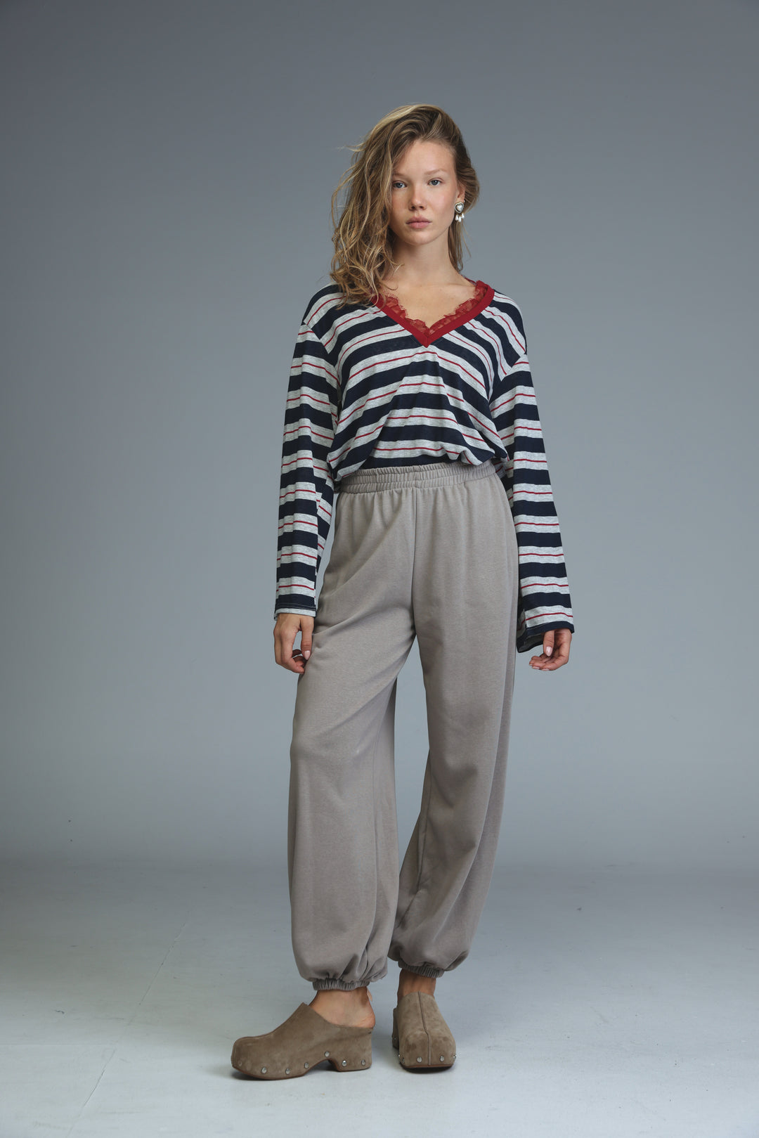 A woman wearing beige joggers paired with a long-sleeved navy and white striped top with a red lace-trimmed v-neckline
