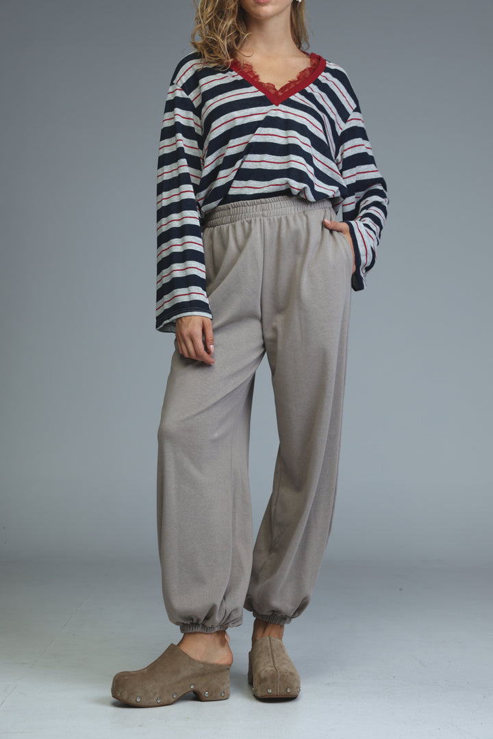 A woman wearing beige joggers with a front view and a striped long-sleeve top with red lace trim at the neckline
