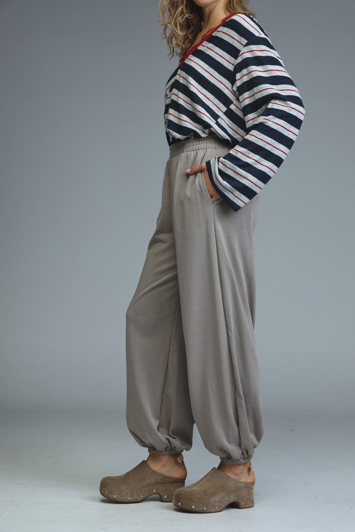 Beige joggers with a loose fit and elastic cuffs shown from the front paired with a striped top and wooden sole shoes