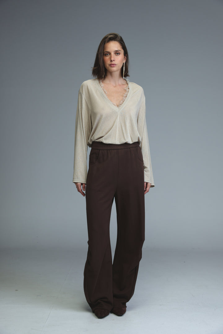 Beige long-sleeved blouse with v-neckline and lace trim shown from the front paired with brown joggers
