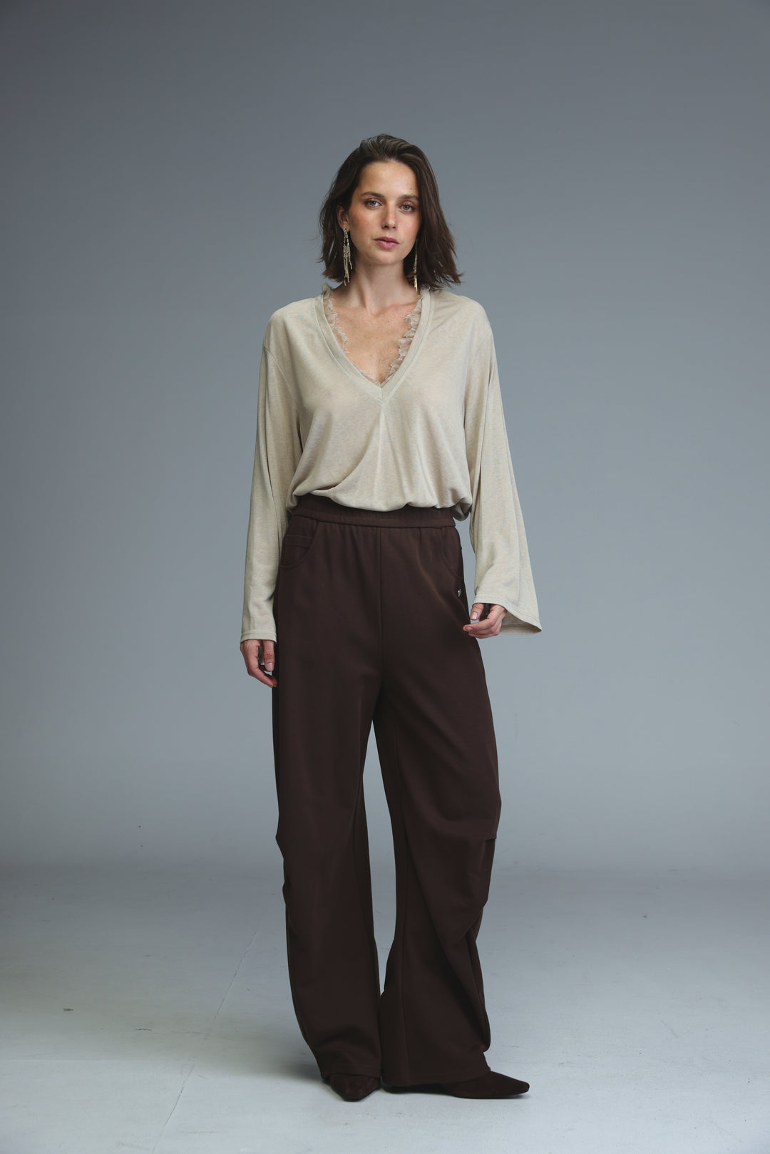Beige long-sleeved blouse with v-neckline and delicate lace trim shown from the front paired with brown joggers