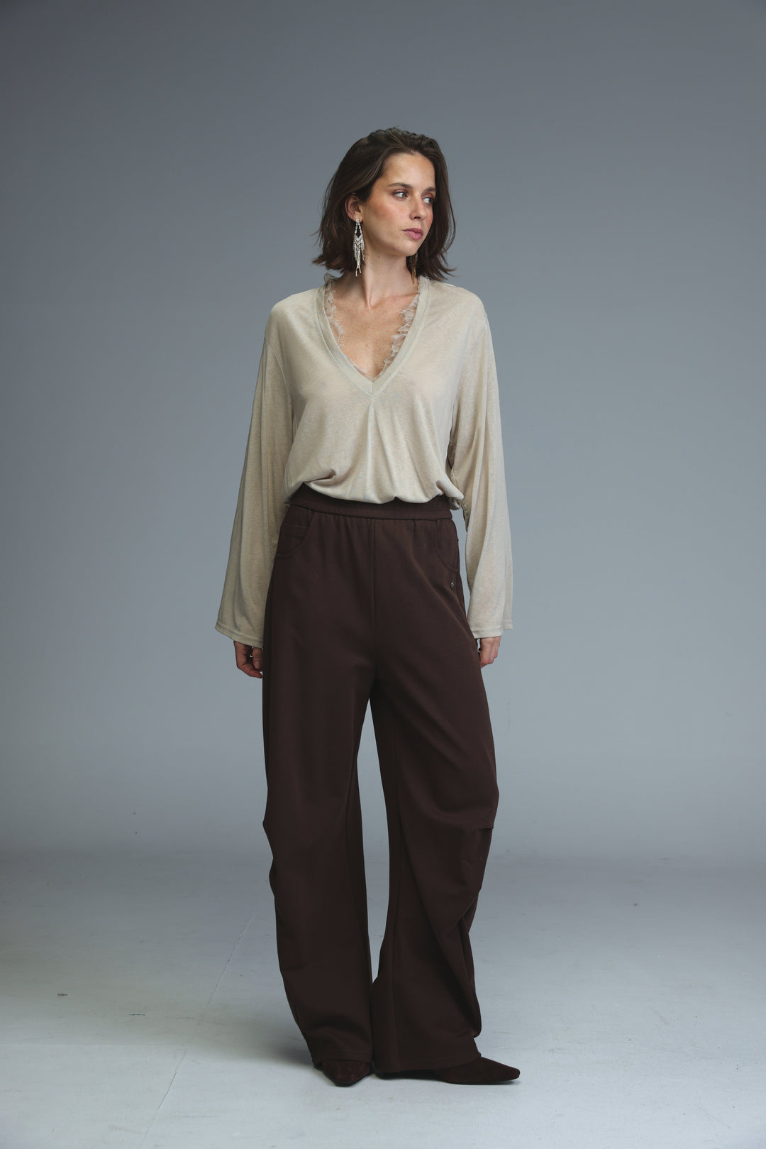 Brown joggers with an elastic waistband paired with a beige v-neck blouse featuring long sleeves and beaded neck detailing