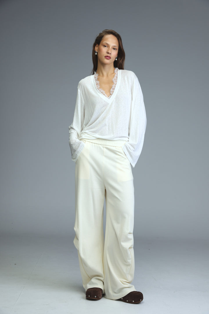 Cream joggers paired with a white blouse featuring delicate lace trim at the neckline shown from the front