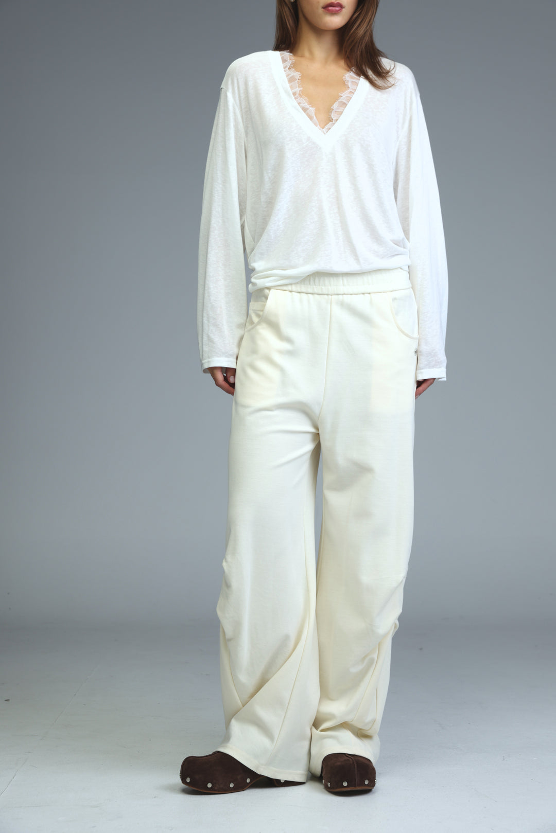 A woman wearing cream 646 joggers with wide legs paired with a white long-sleeved v-neck top with lace trim and brown shoes