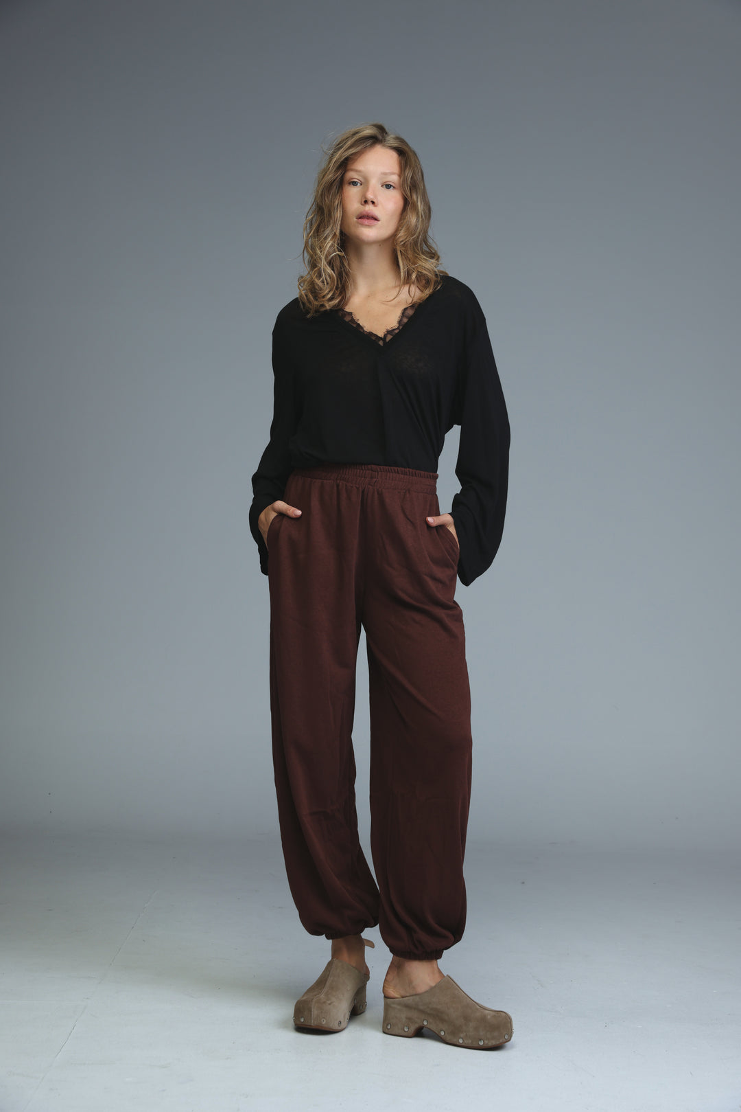 A woman wears brown joggers with loose fit paired with a black blouse and beige platform clogs in a front view