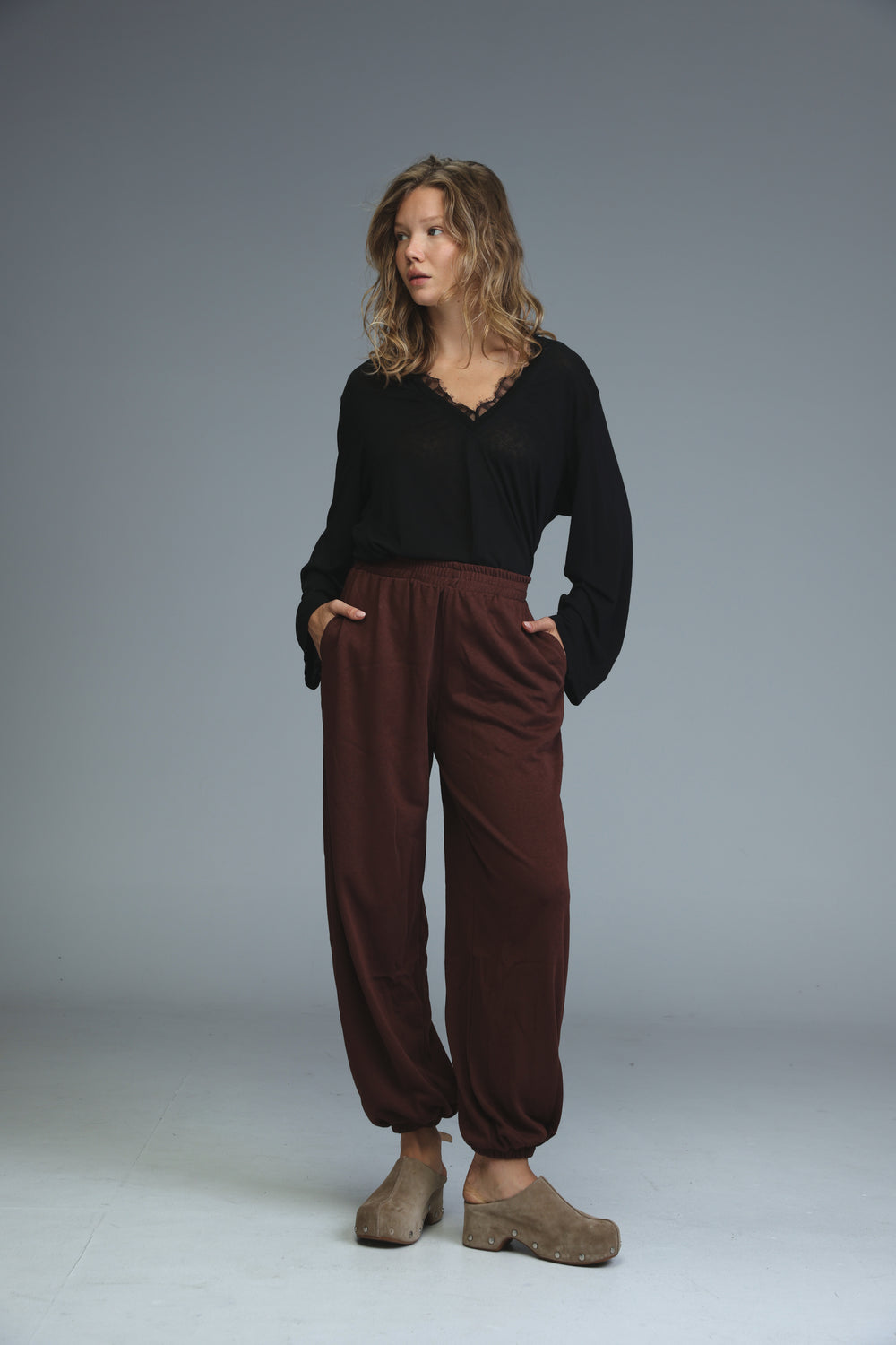 The model is wearing soft dark brown loose-fitting joggers with elasticated cuffs shown from the front