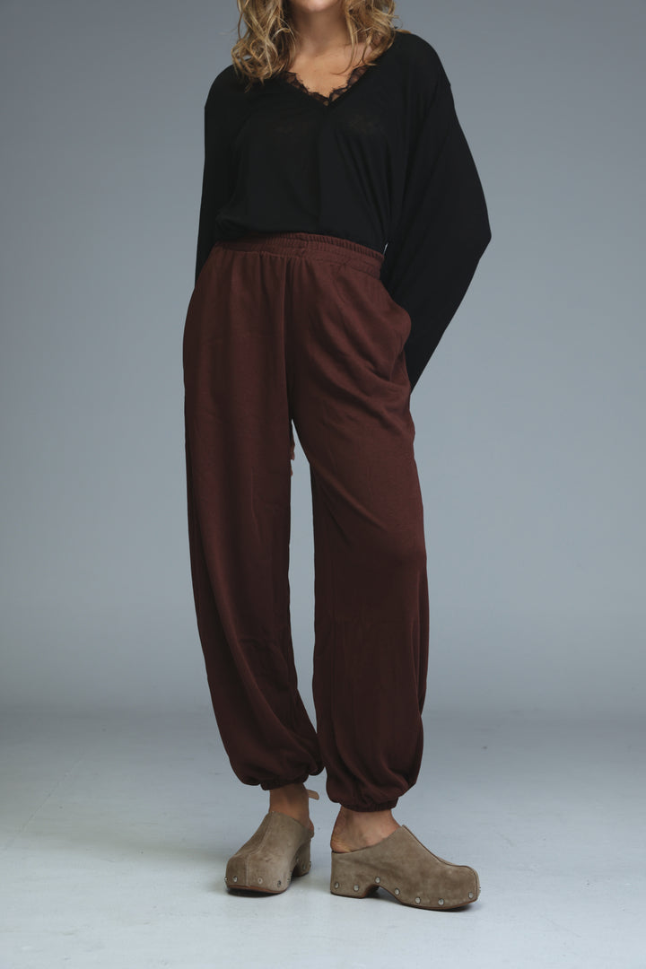 Brown loose-fitting harem pants with elastic waistband and cuffed ankles shown from the front