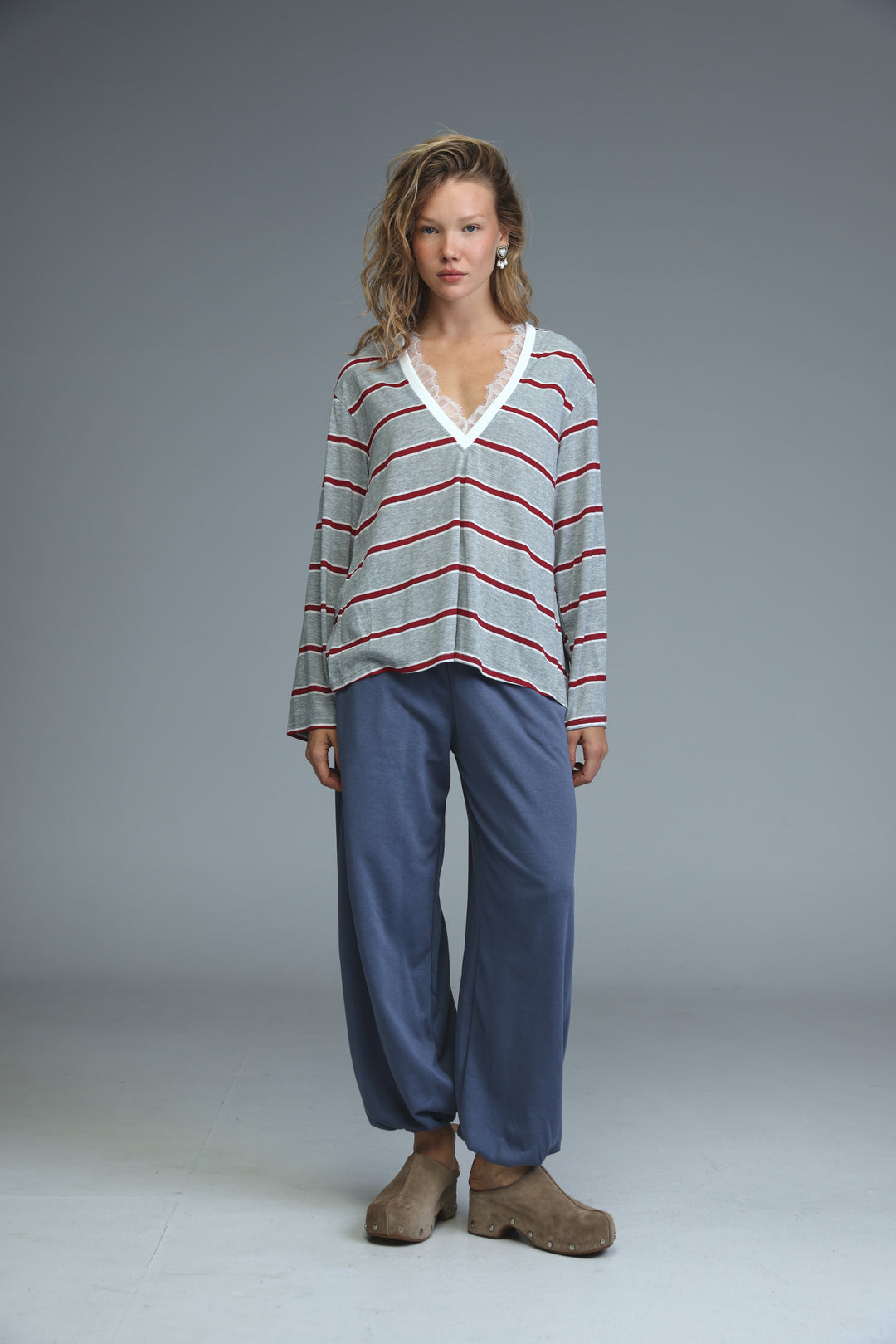 A woman wears a glow grey long-sleeved v-neck shirt with horizontal gray and red stripes and white lace trim