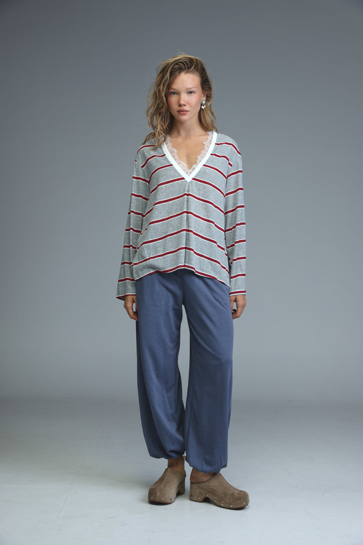 A woman wears a glow grey long-sleeved v-neck shirt with horizontal gray and red stripes and white lace trim