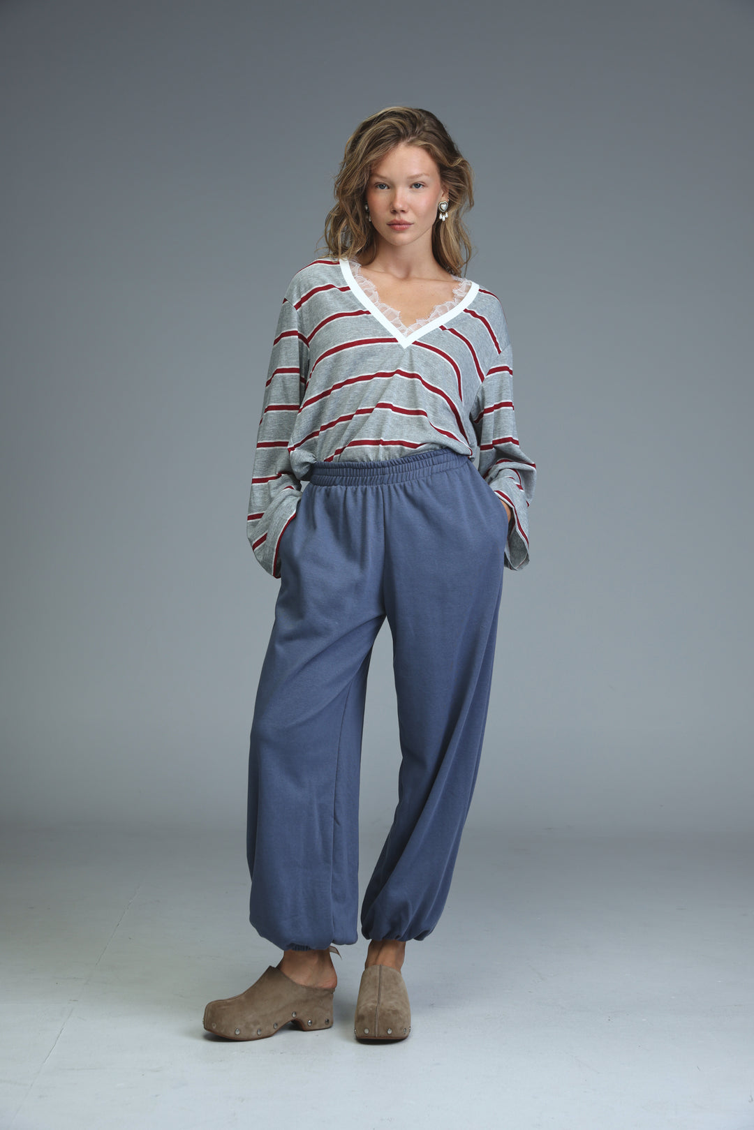 Woman wearing blue wide-leg joggers paired with gray and red striped v-neck top with white lace trim front view
