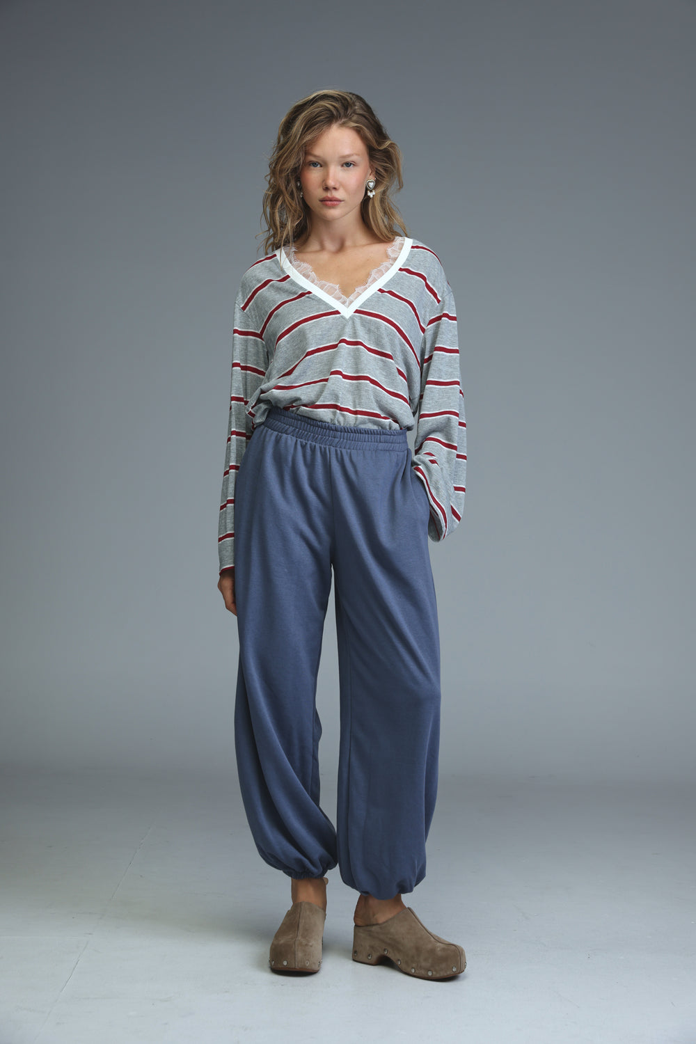 A woman wearing a front view gray striped glow shirt with red stripes and white lace v-neckline trim paired with navy pants