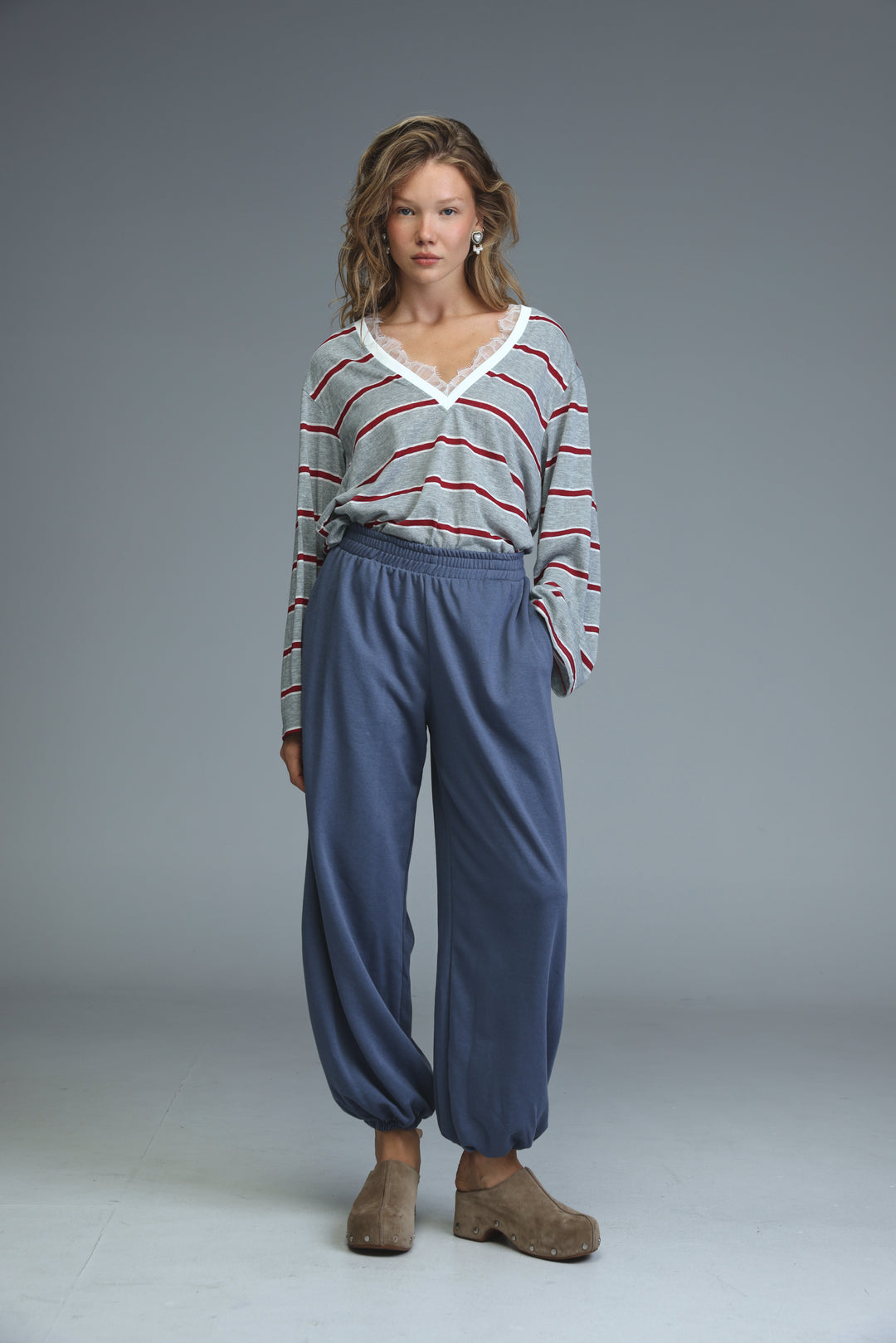A woman wearing a front view gray striped glow shirt with red stripes and white lace v-neckline trim paired with navy pants