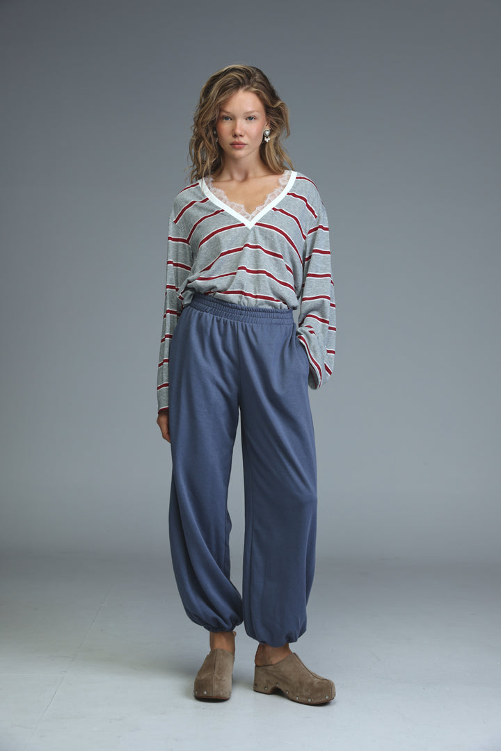A woman wearing a front view gray striped glow shirt with red stripes and white lace v-neckline trim paired with navy pants