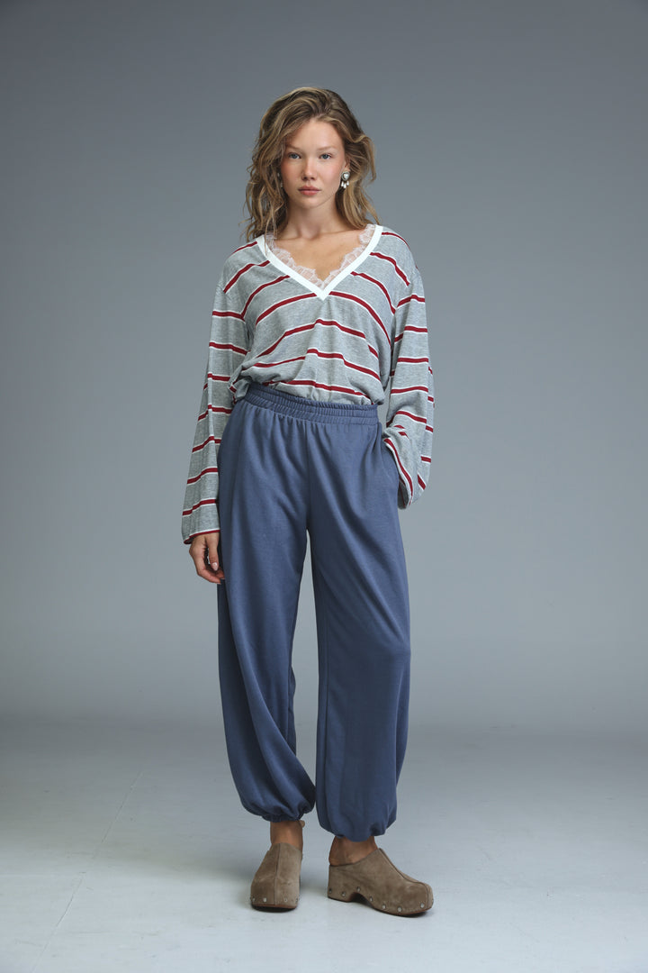 A woman wearing navy blue drawstring joggers paired with a gray and red striped long-sleeved top with white lace trim