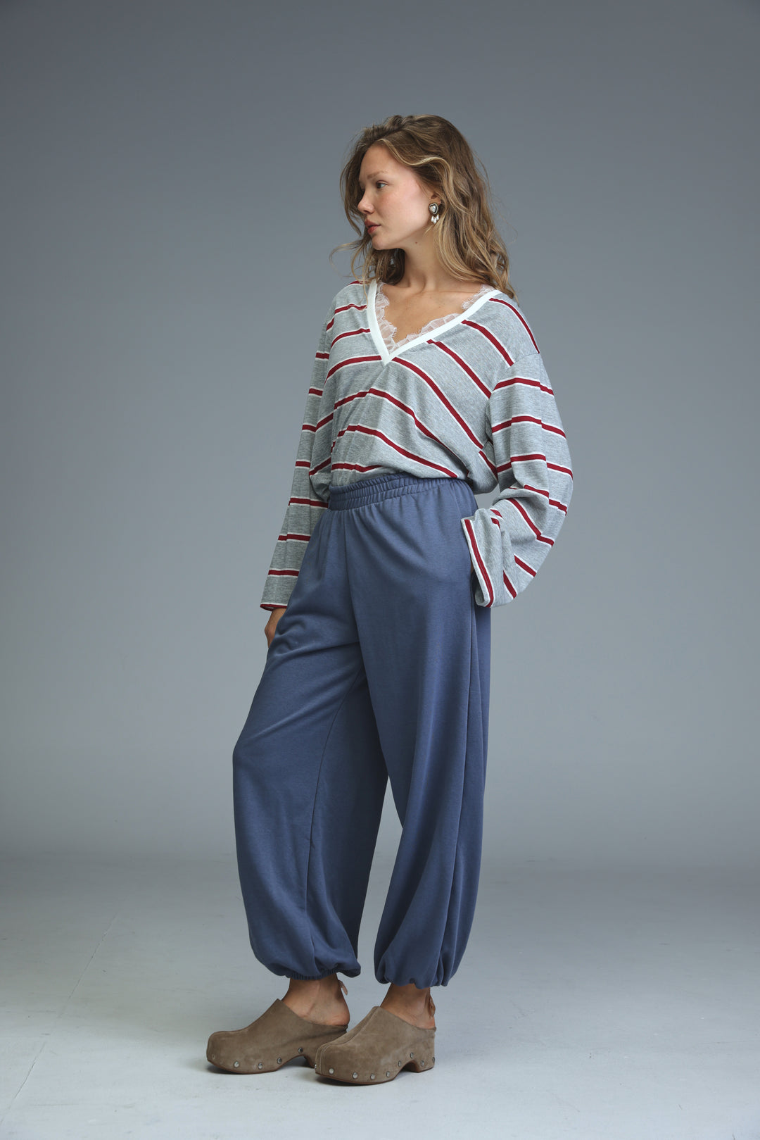 Woman wearing try blue joggers with loose fit paired with gray and red striped long-sleeved top with lace neckline