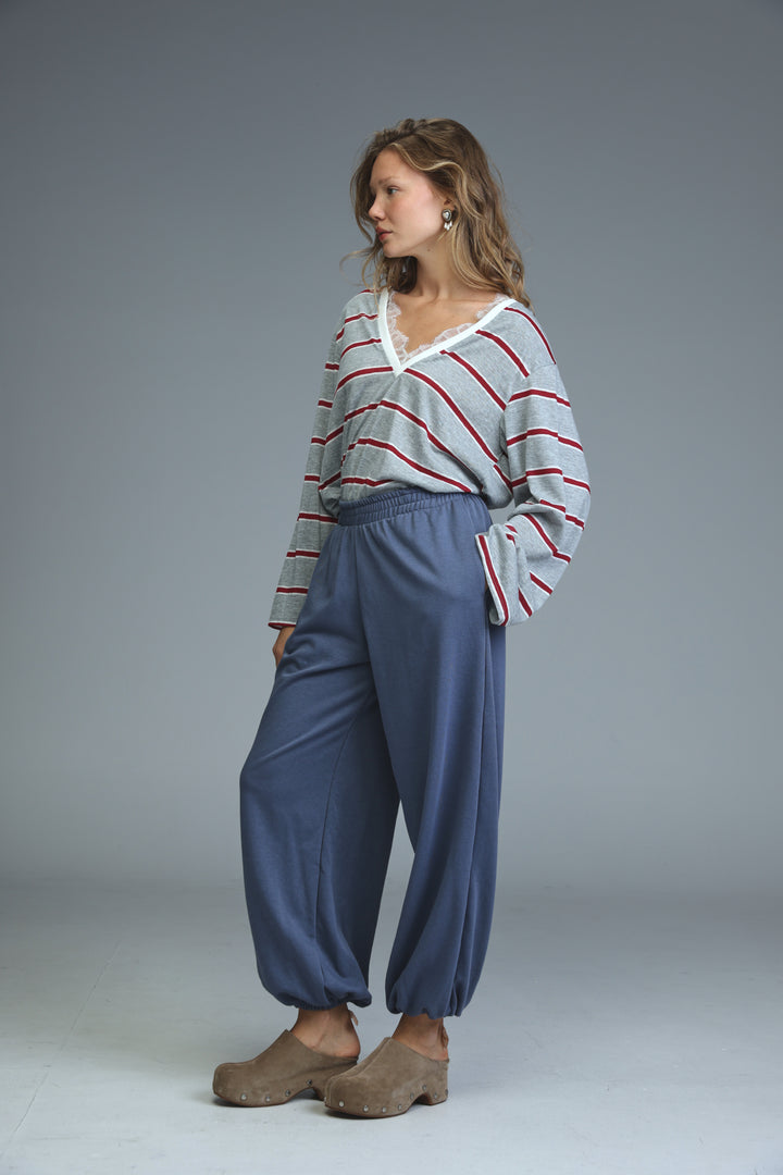 Woman wearing try blue joggers with loose fit paired with gray and red striped long-sleeved top with lace neckline
