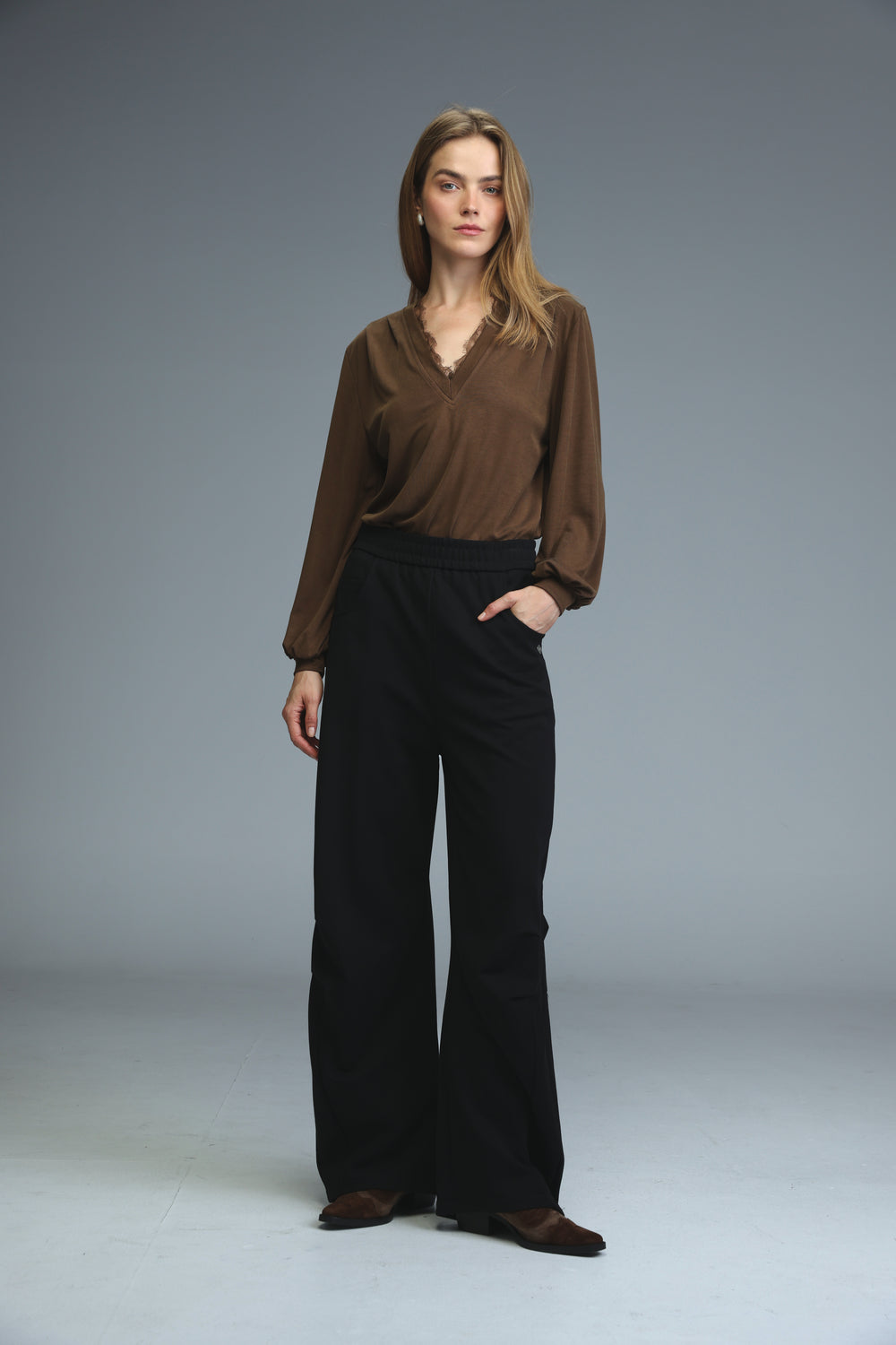 A woman wears black joggers with a brown long-sleeved blouse featuring a subtle v-neckline and sheer fabric front view