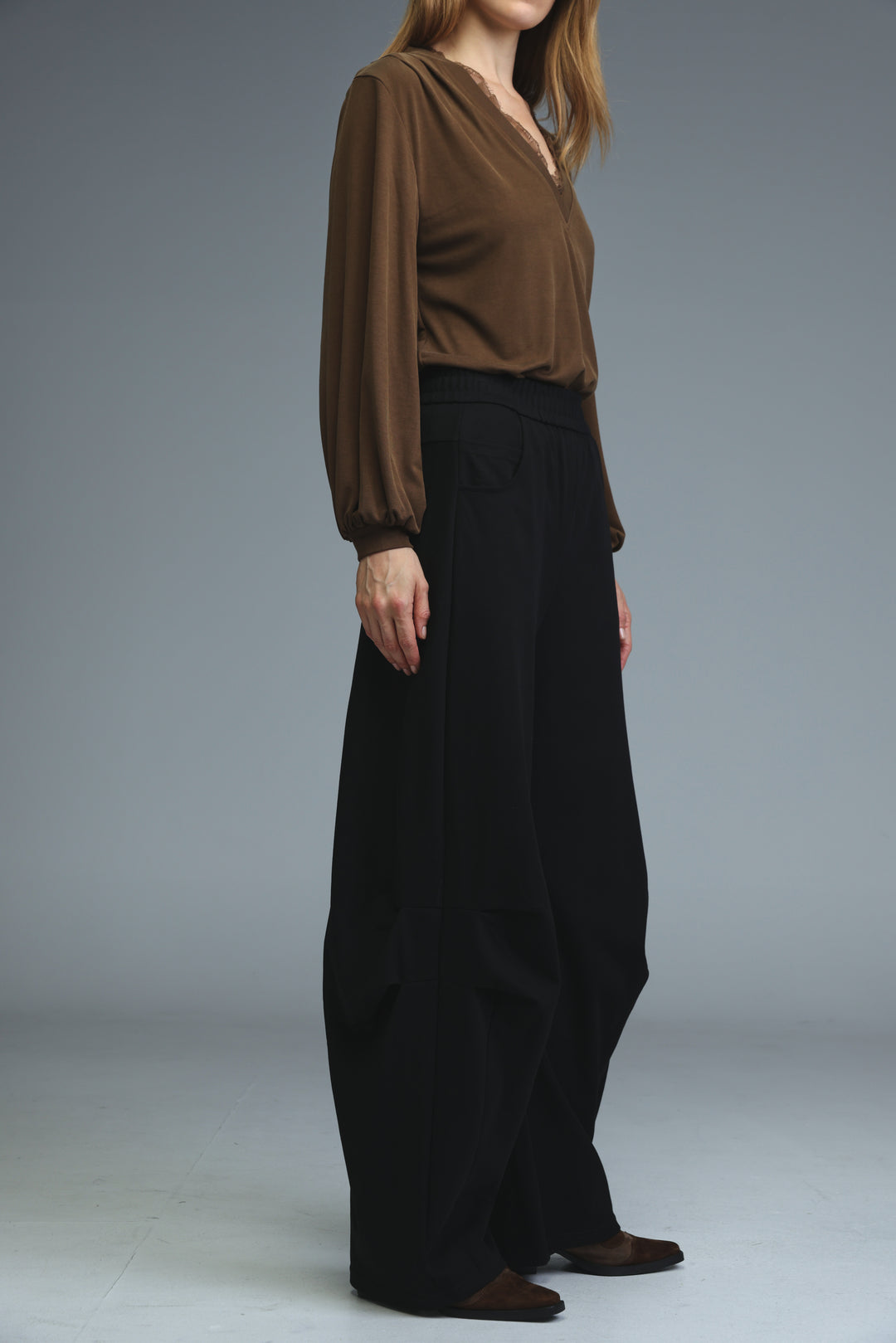 A woman wearing 646 black joggers with high-waisted wide-leg fit and a brown long-sleeved v-neck blouse visible from the front