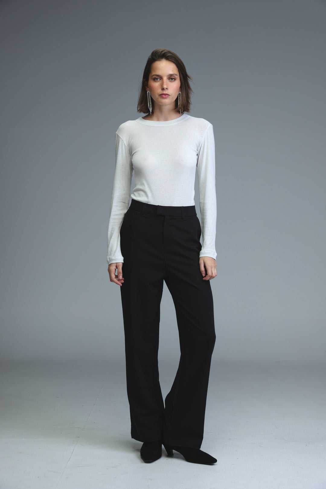 A front view of mid rise tailored black flared trousers paired with a sleek white long-sleeved top
