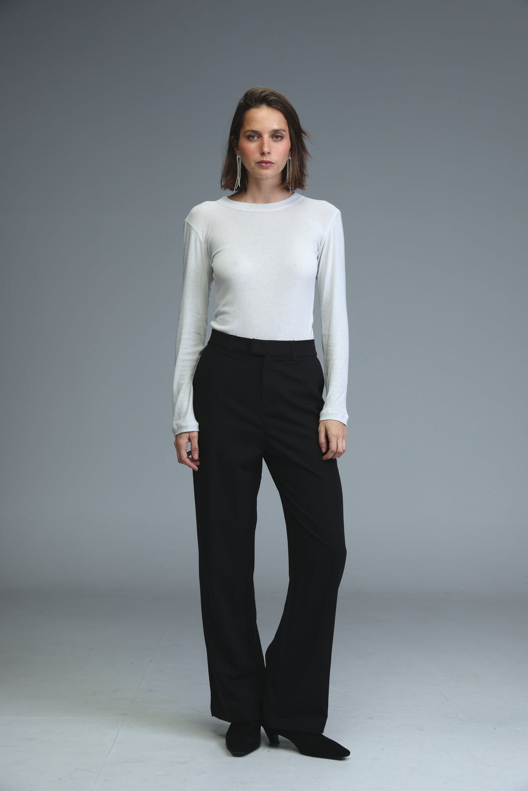 Mid rise tailored black bottoms paired with a minimalist white long-sleeved top with round neckline and shoulder seams front view