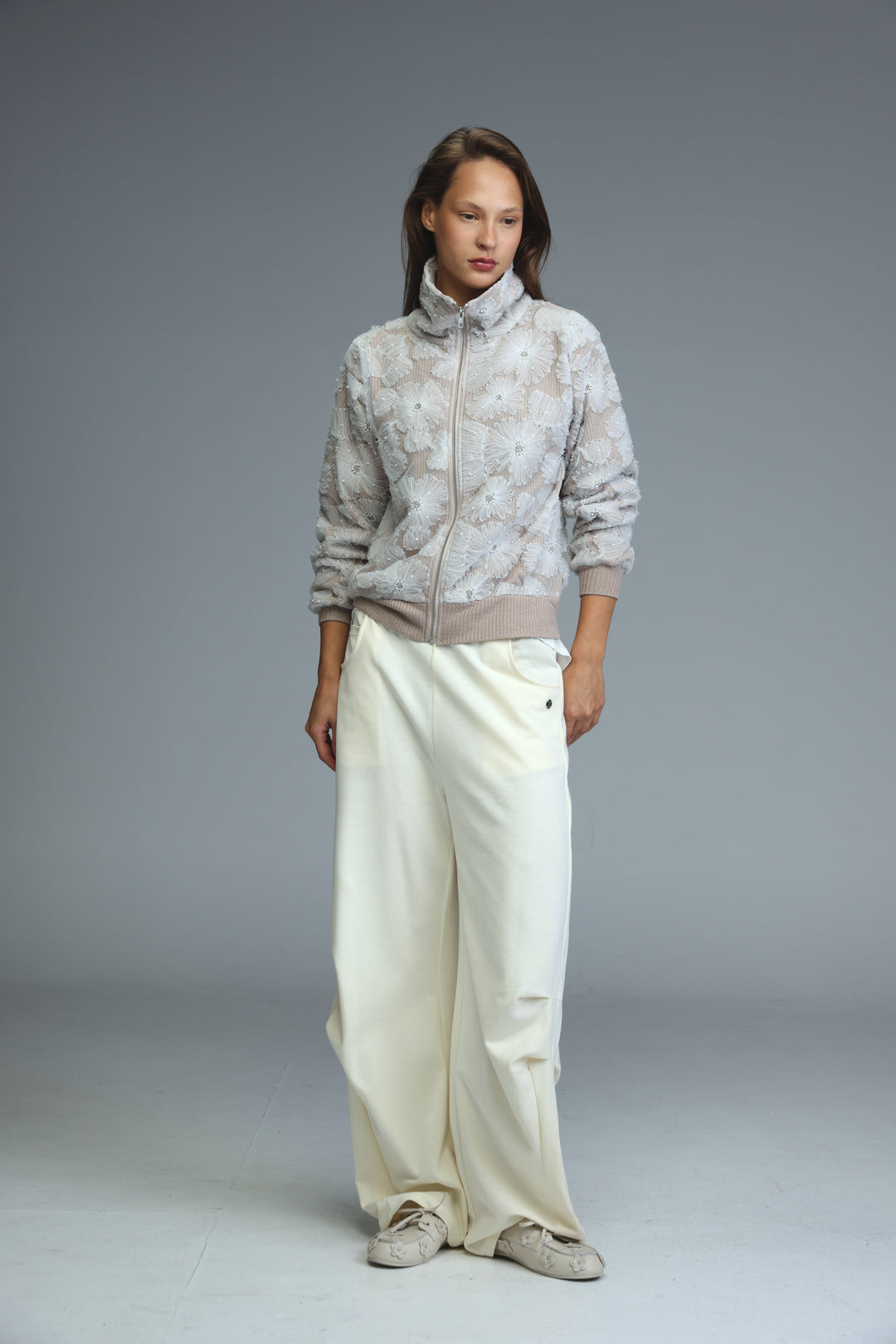A woman wearing a light gray blossom stone jacket with floral embroidery and beige ribbed cuffs, front view