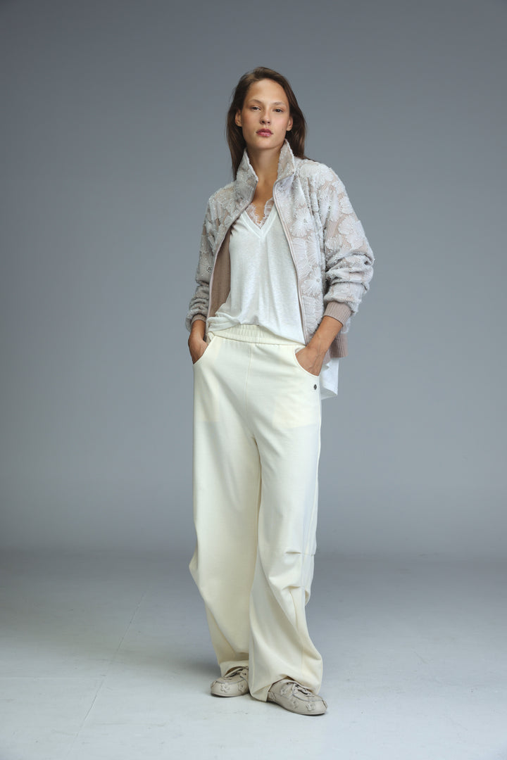 A woman wearing a light gray Blossom Stone quilted bomber jacket with a subtle snakeskin pattern and white trousers