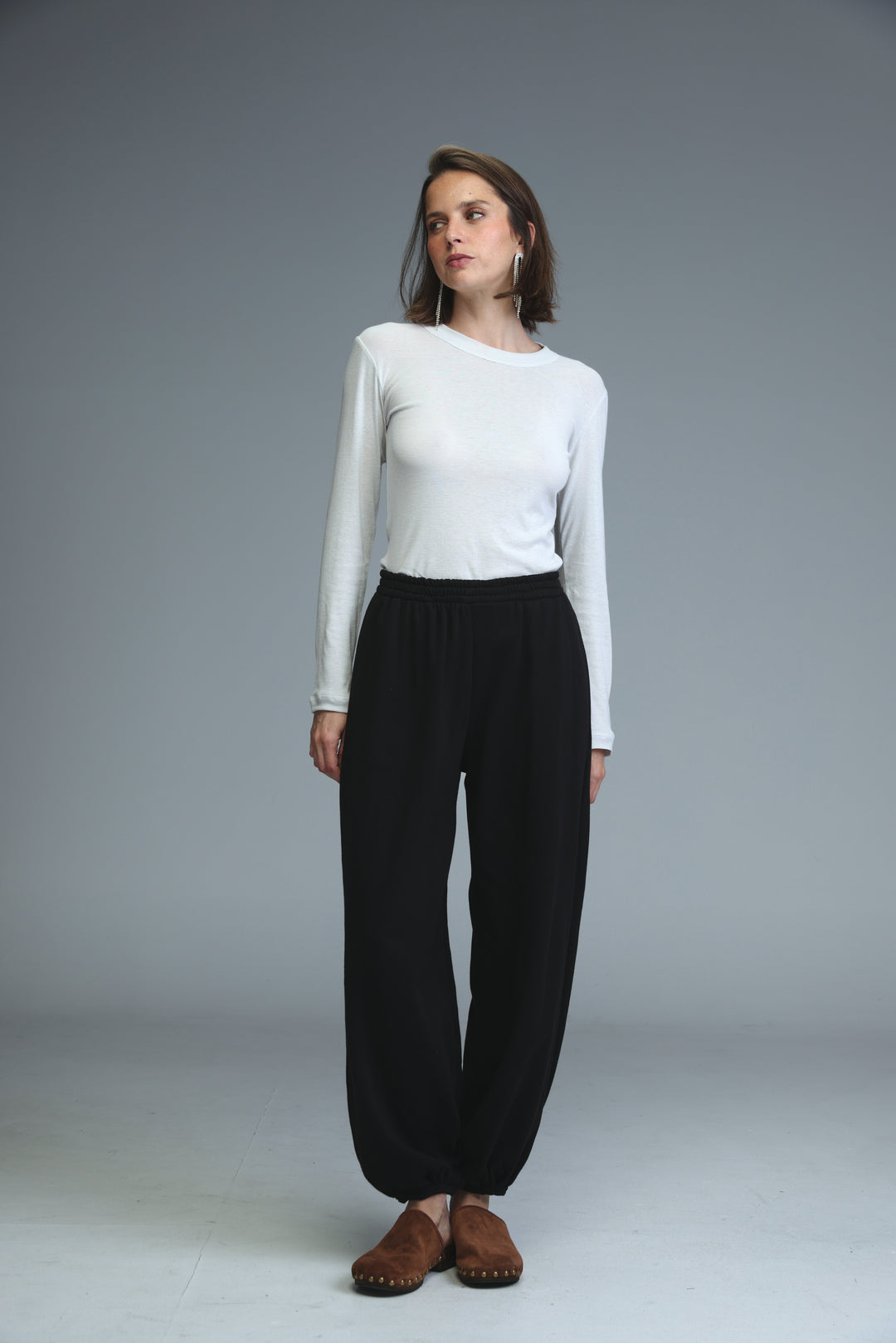 A woman wears black high-waisted wide-leg joggers paired with a white long-sleeved top and brown moccasins